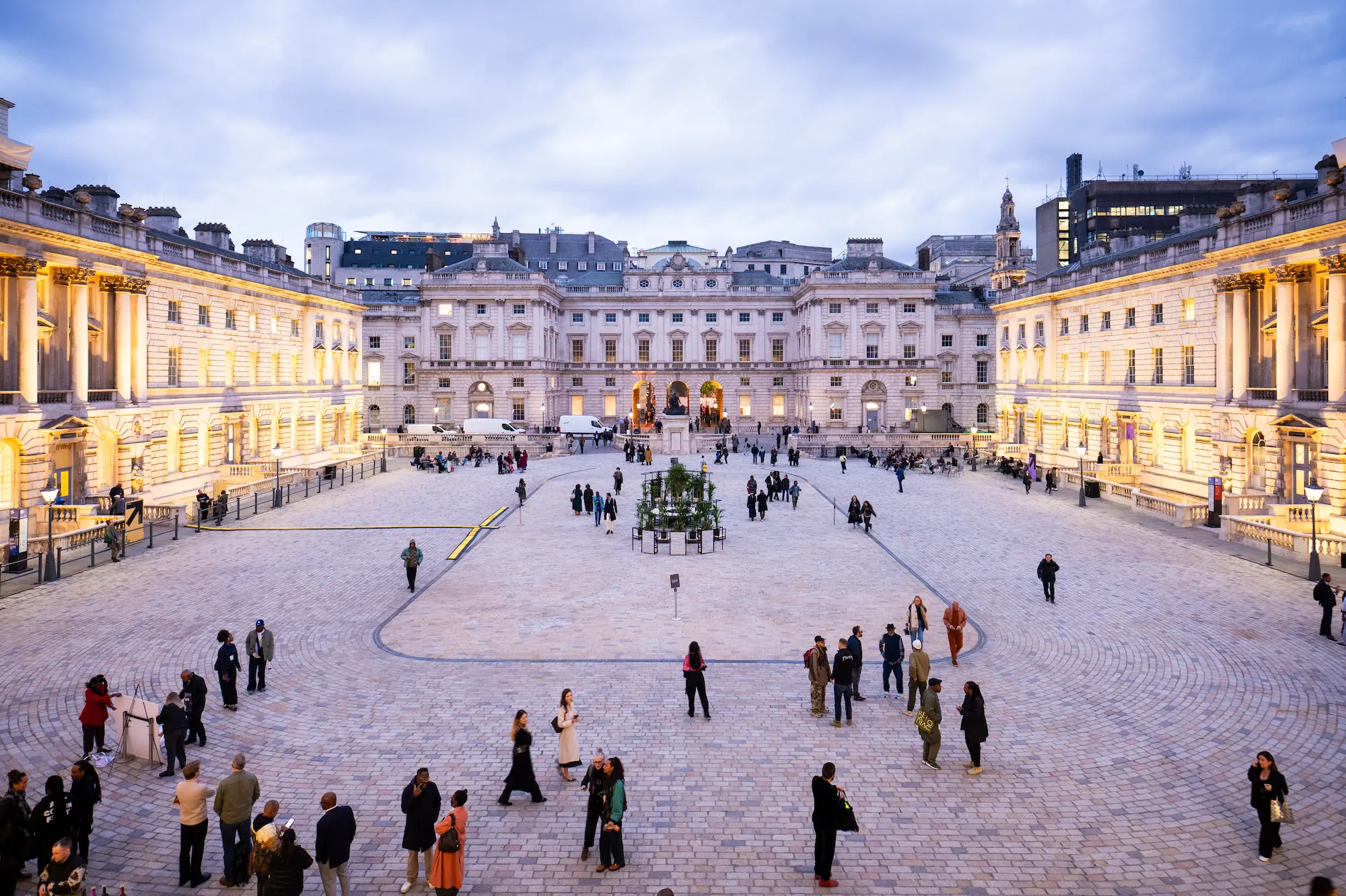 Wide view of the illuminated Somerset House courtyard in London at dusk, filled with visitors attending the 1-54 Contemporary African Art Fair 2025, showcasing the venue’s grand neoclassical architecture and vibrant cultural atmosphere.