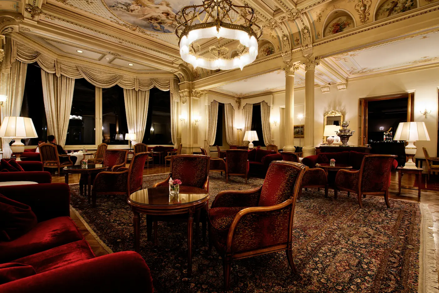 A luxurious hotel lounge with ornate ceilings, velvet armchairs, golden chandeliers, and richly decorated drapes, exuding timeless European elegan