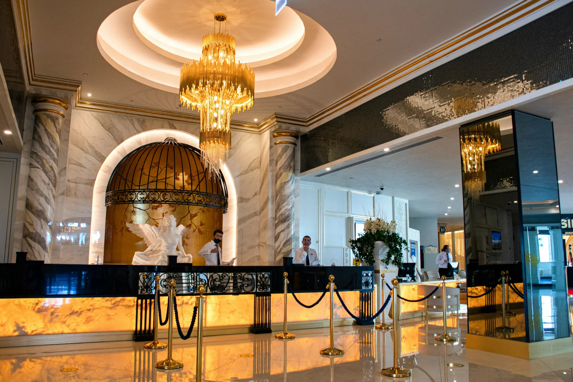 Elegant hotel reception area featuring a golden chandelier, marble columns, and a warmly lit front desk, evoking a luxurious and refined atmosphere.