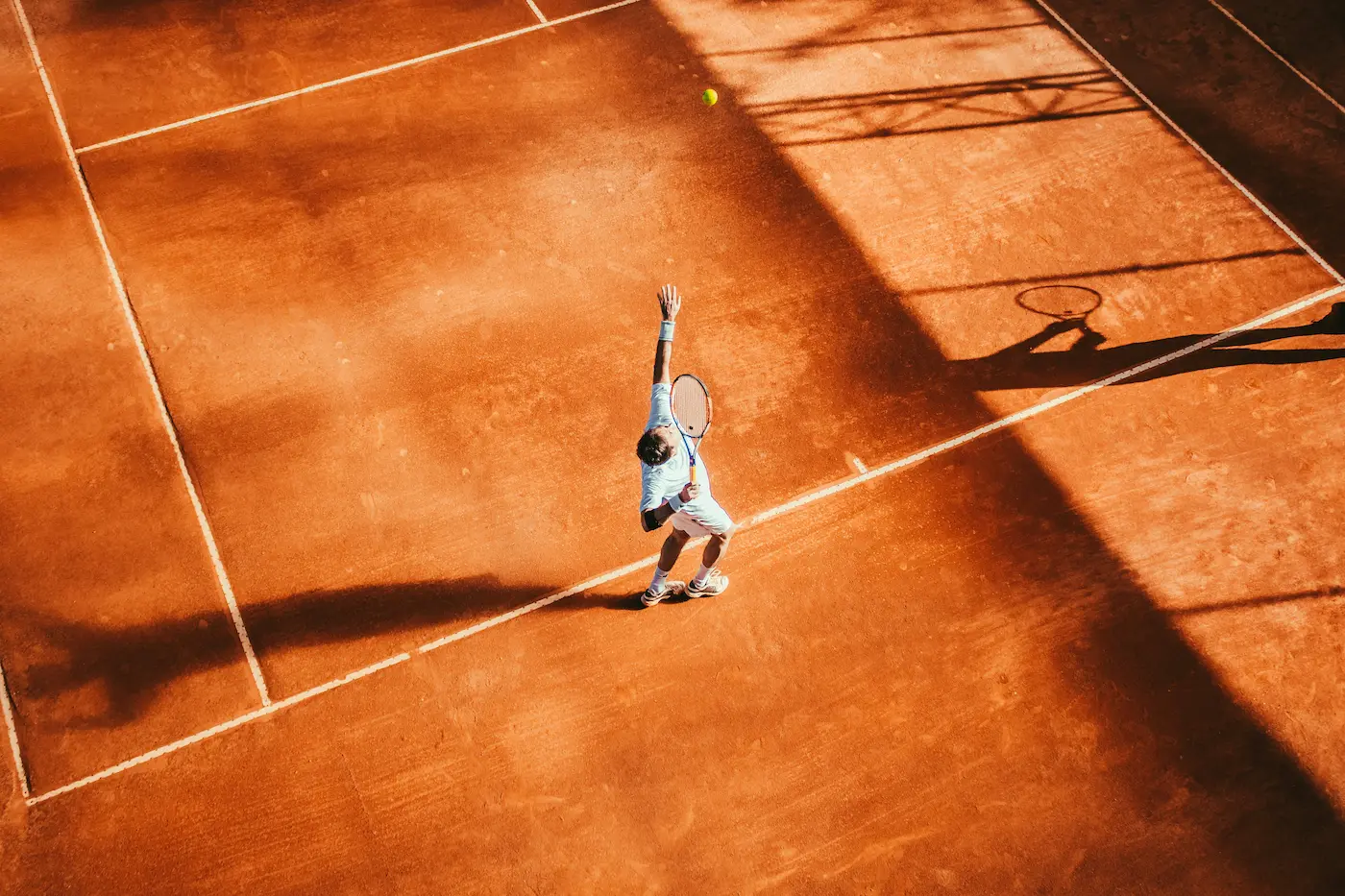 A tennis player captured mid-serve on a sunlit clay court, with dynamic shadows and precise motion conveying the intensity of the match.