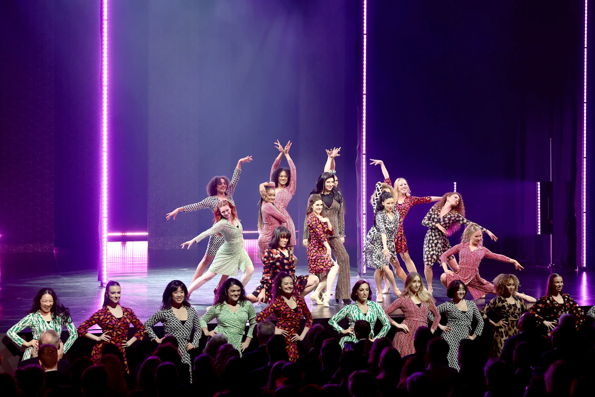Group of dancers performing on stage in colorful wrap dresses during the PAC NYC Icons of Culture Gala 2025, celebrating Diane von Furstenberg’s iconic fashion legacy under vibrant purple lighting.