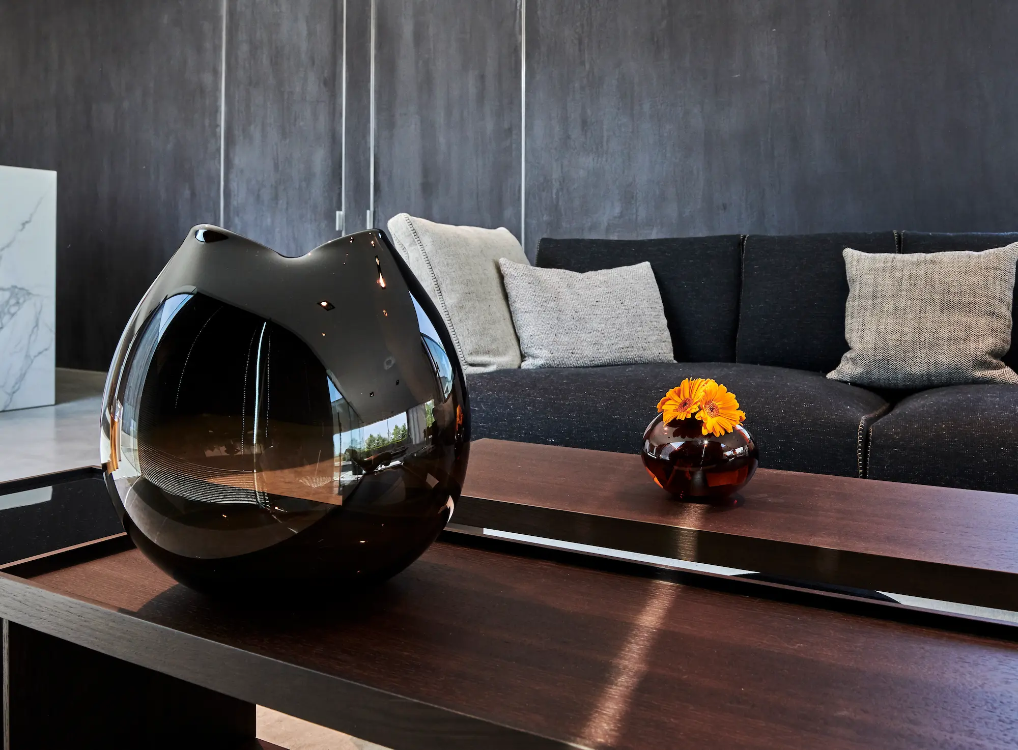 Close-up of two sculptural glass vases by When Objects Work on a dark wooden coffee table, styled in a modern minimalist living room with a dark sofa and neutral cushions.