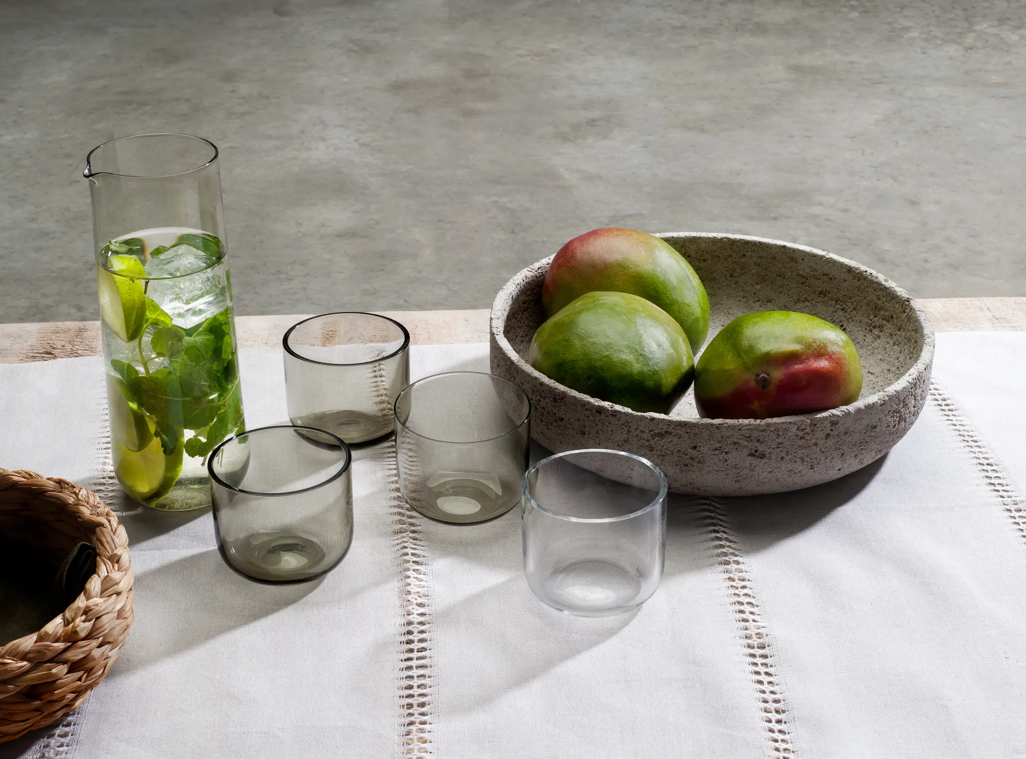 Elegant tabletop scene featuring When Objects Work glassware and a textured stone bowl filled with mangoes, styled on a neutral linen tablecloth with natural light.