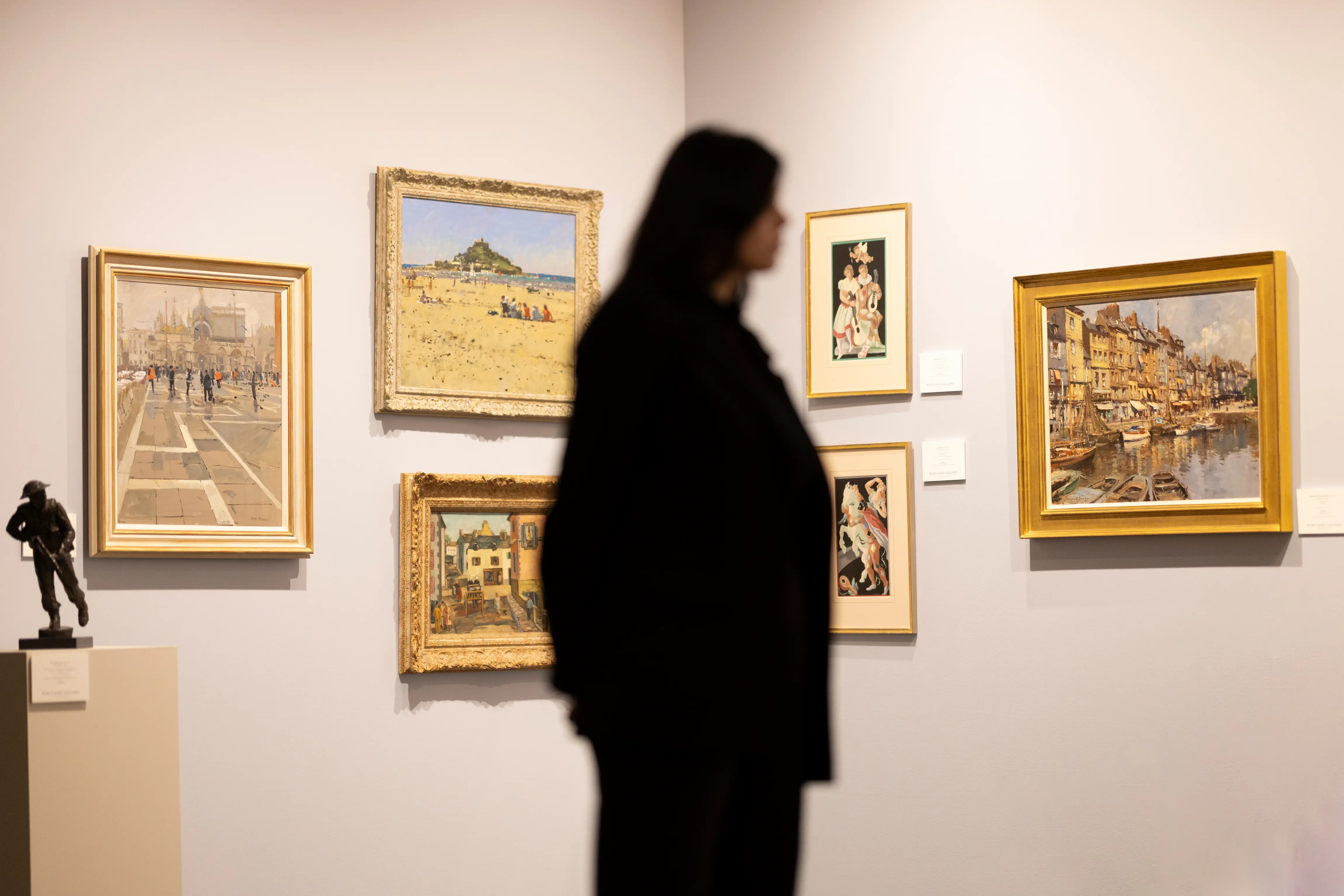 A visitor observes a collection of framed paintings and sculptures displayed at the LAPADA Art & Antiques Fair 2025 in Berkeley Square, London.