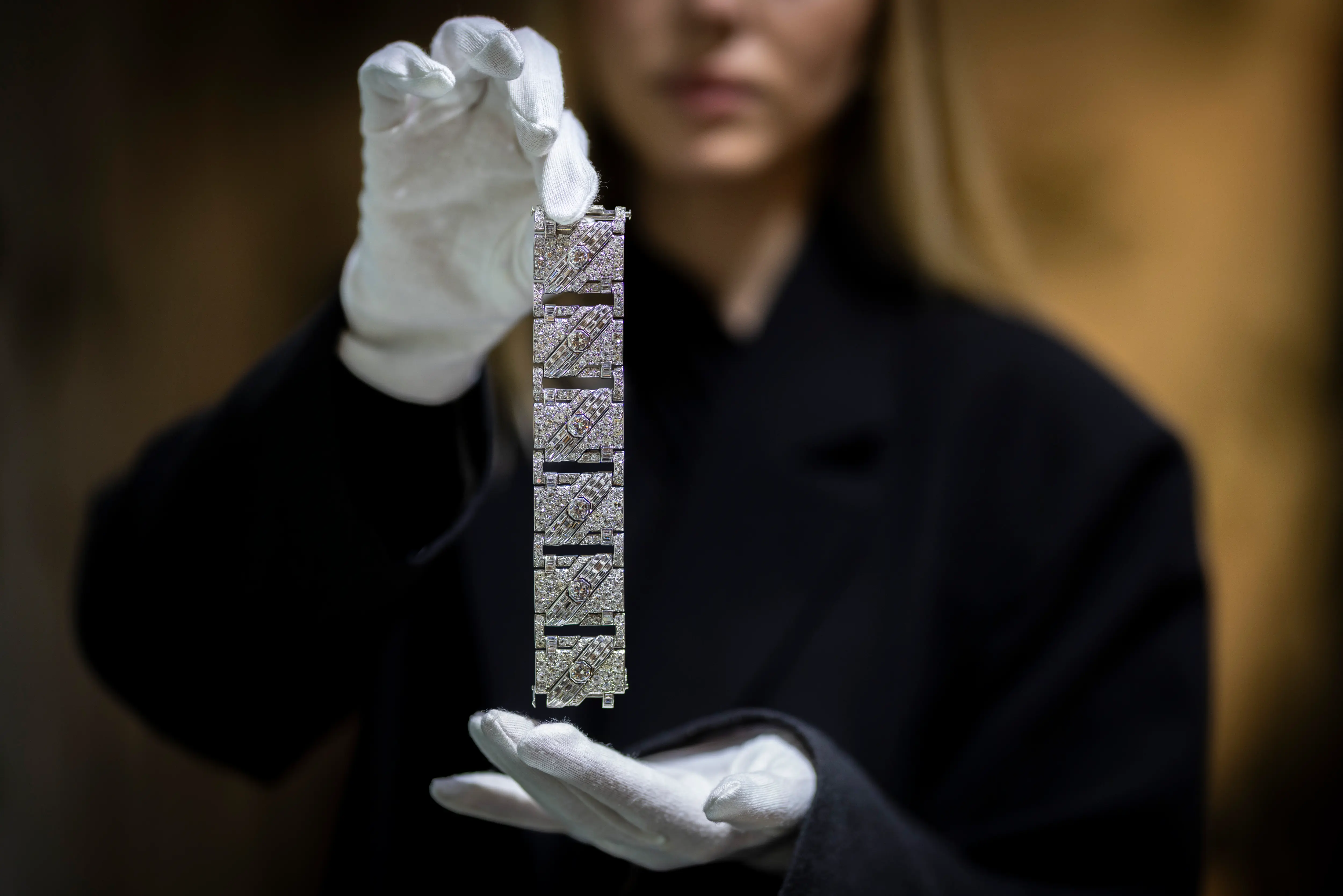 A curator wearing white gloves holds an intricate Art Deco diamond bracelet on display at the LAPADA Art & Antiques Fair 2025 in Berkeley Square, London, presented by Koopman Rare Art.