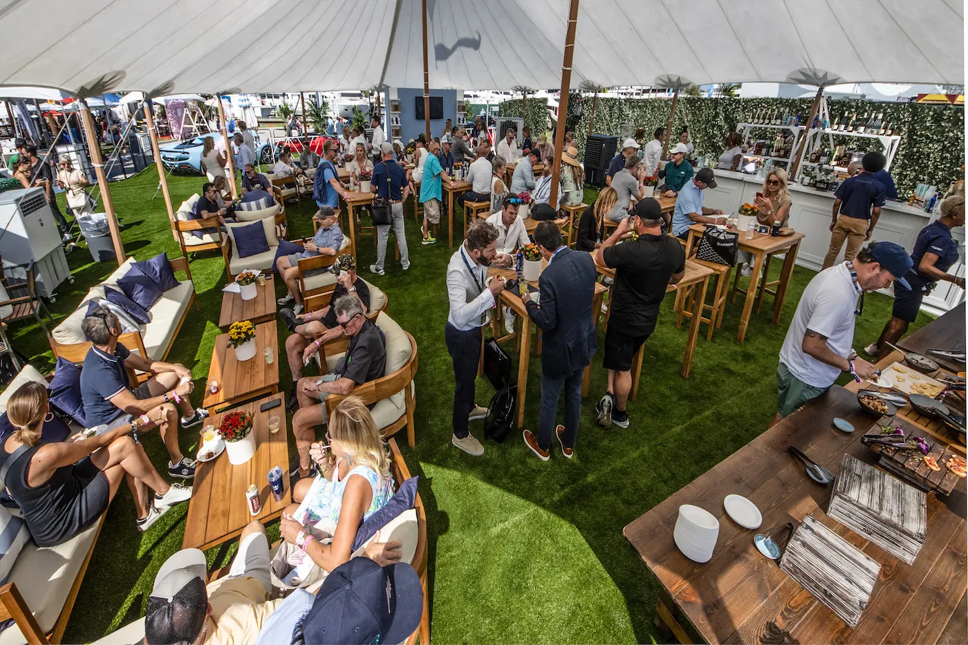 Guests relax and mingle under a shaded canopy at the Windward VIP Lounge during the 2025 Fort Lauderdale International Boat Show, enjoying food, drinks, and waterfront views.