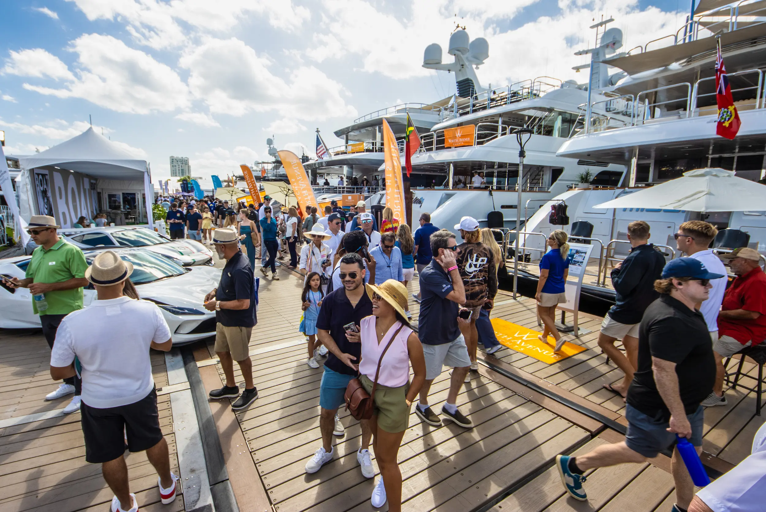 Visitors stroll along the docks lined with luxury yachts and supercars at the 2025 Fort Lauderdale International Boat Show under a bright Florida sky.