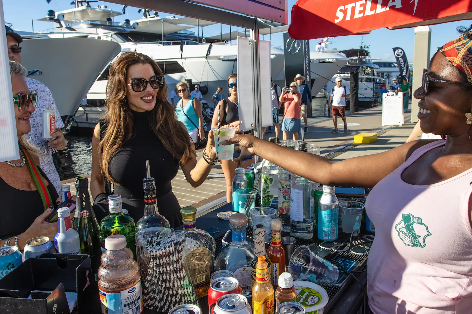 A bartender serves a smiling guest a cocktail at the Goslings Island Bar during the 2025 Fort Lauderdale International Boat Show, surrounded by bottles and waterfront views.
