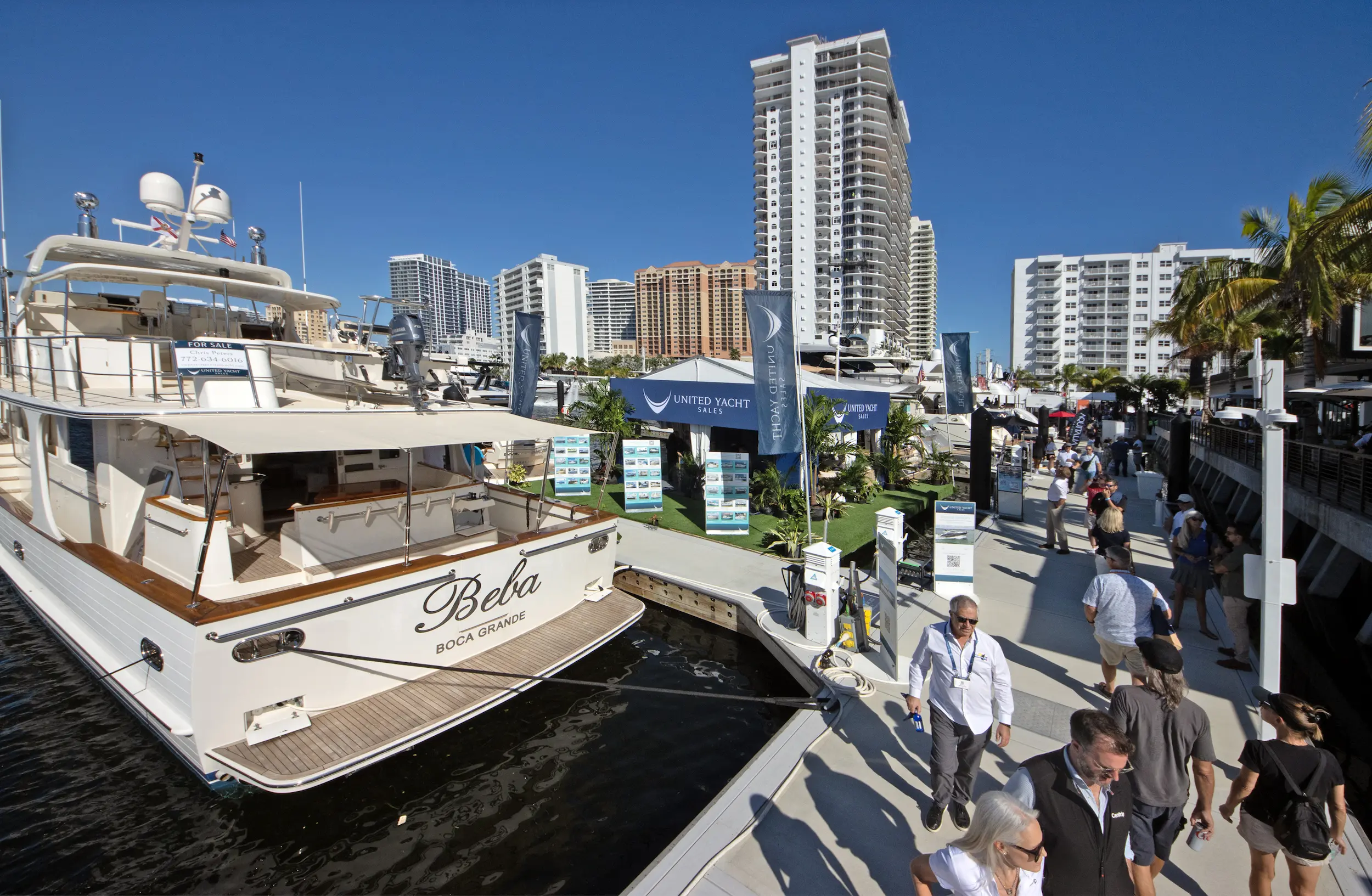 Visitors walk along the marina lined with luxury yachts and exhibitor tents under clear blue skies at the 2025 Fort Lauderdale International Boat Show.