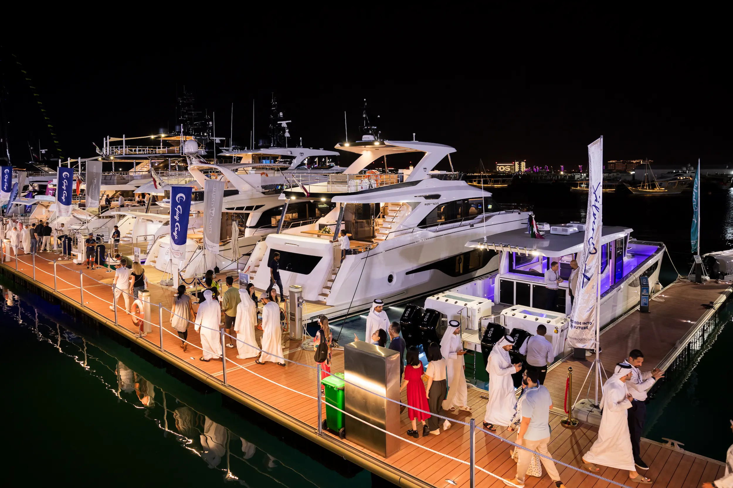 Guests stroll along the illuminated marina at Old Doha Port, viewing luxury yachts during the Qatar Boat Show 2025 under the night sky in Doha, Qatar.