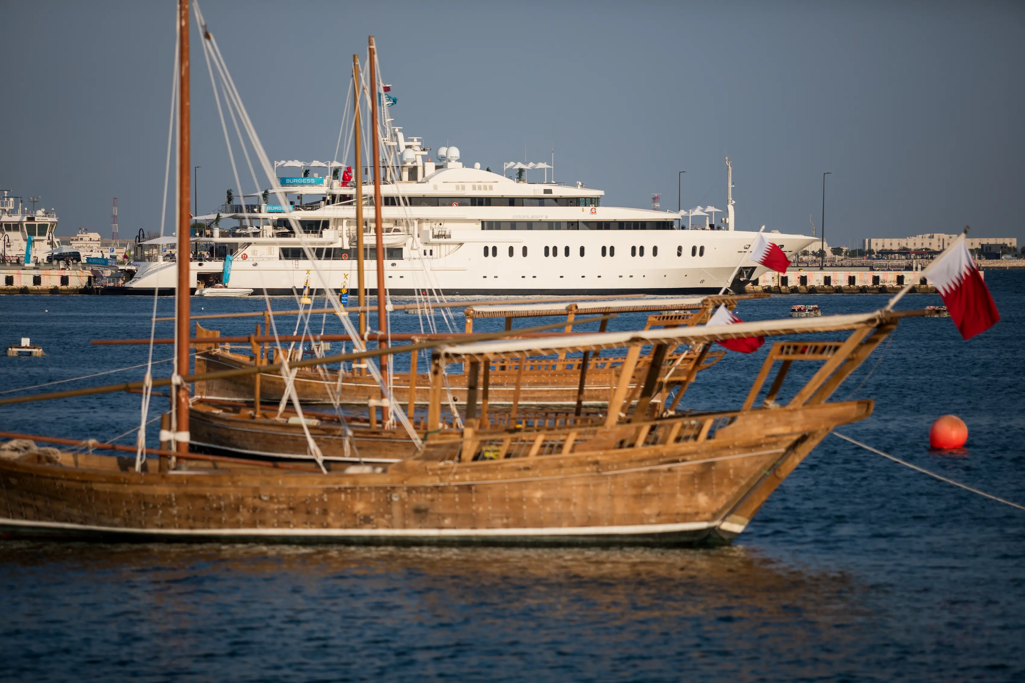Wooden dhows adorned with Qatari flags float in front of modern luxury yachts at Old Doha Port during the Qatar Boat Show 2025, symbolizing Qatar’s blend of maritime heritage and innovation.