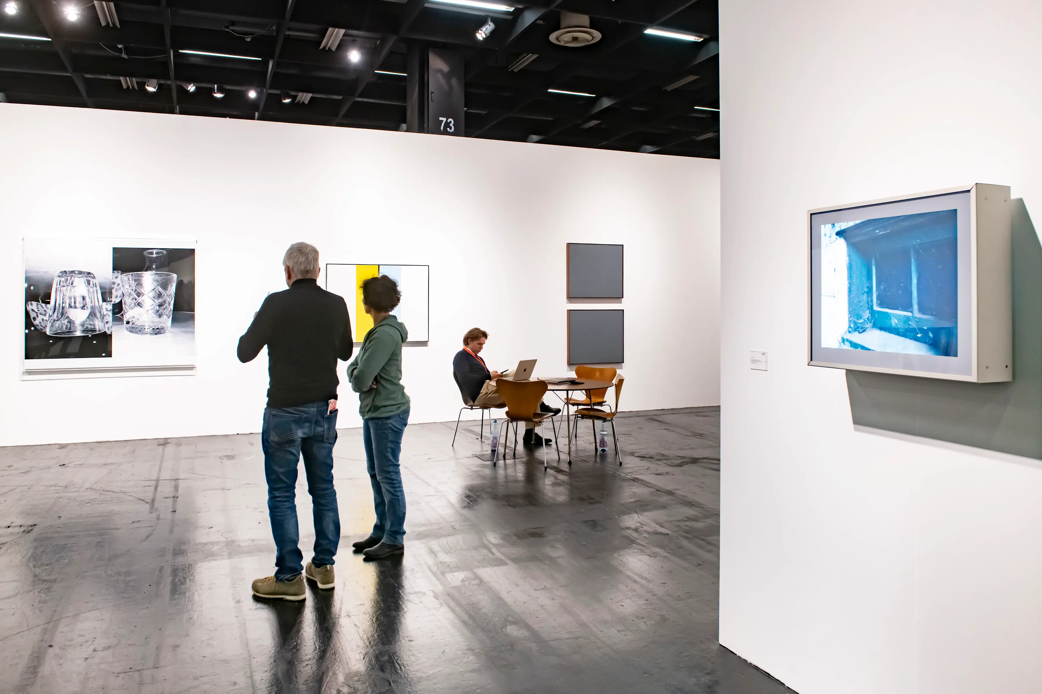 Visitors observe minimalist and photographic artworks displayed in a bright gallery space at Art Cologne 2025, featuring clean compositions and contemporary design elements.