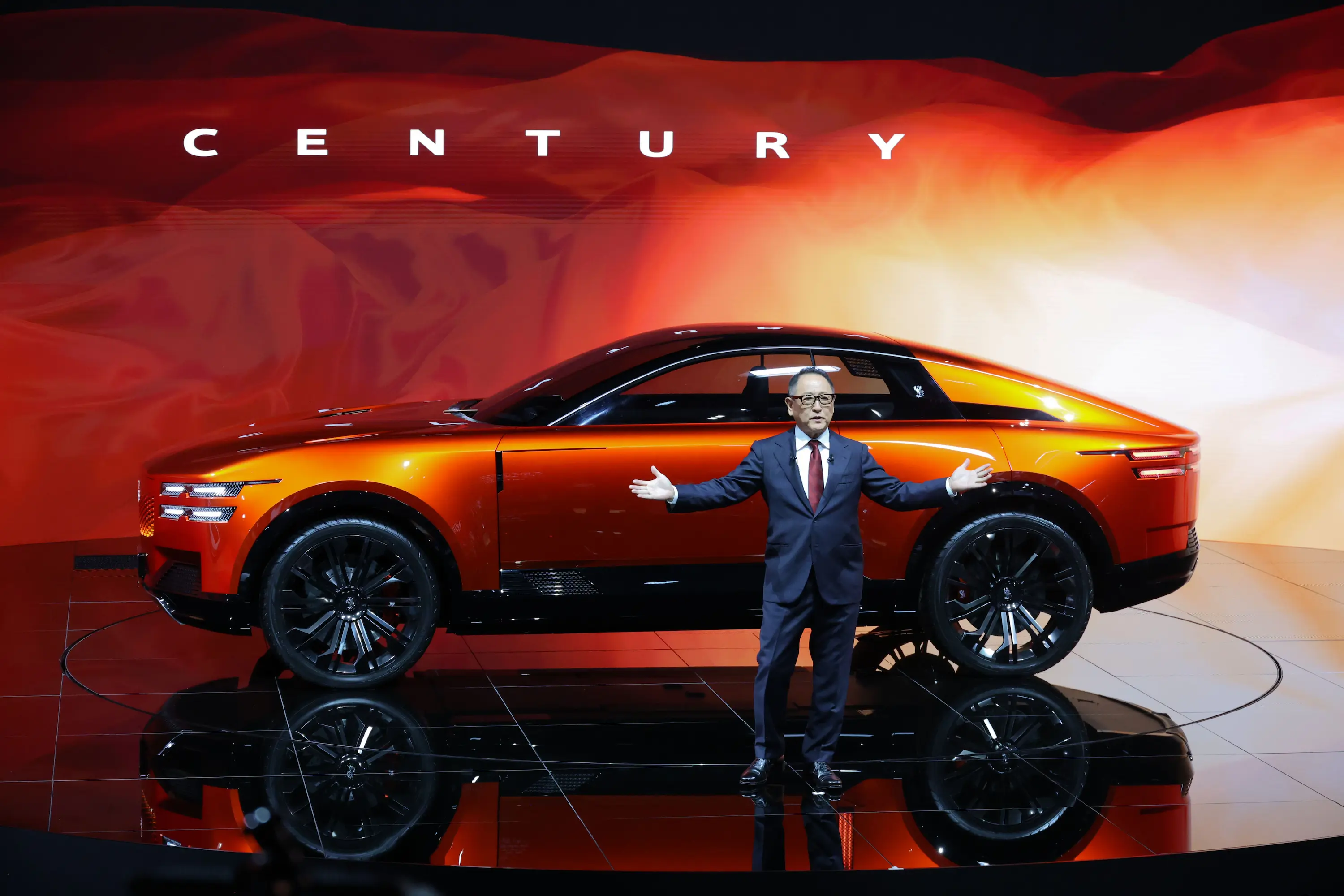 Toyota chairman Akio Toyoda presents the striking orange Century Coupe Concept during the Japan Mobility Show 2025 in Tokyo, showcasing Japan’s vision of ultra-luxury and craftsmanship in future mobility.