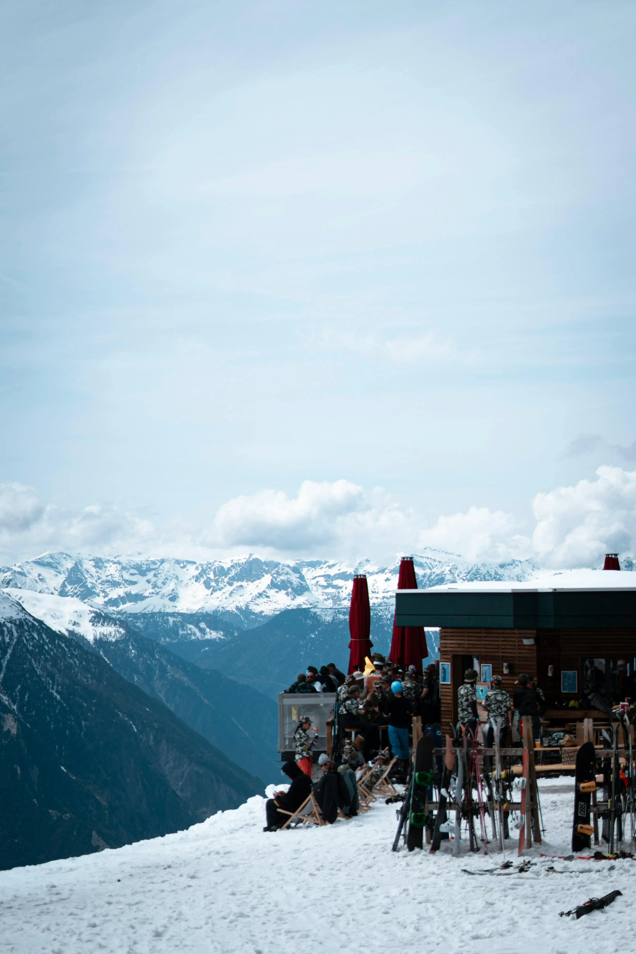 Skiers gathering at mountain hut après-ski terrace with dramatic Swiss alpine panorama and ski equipment