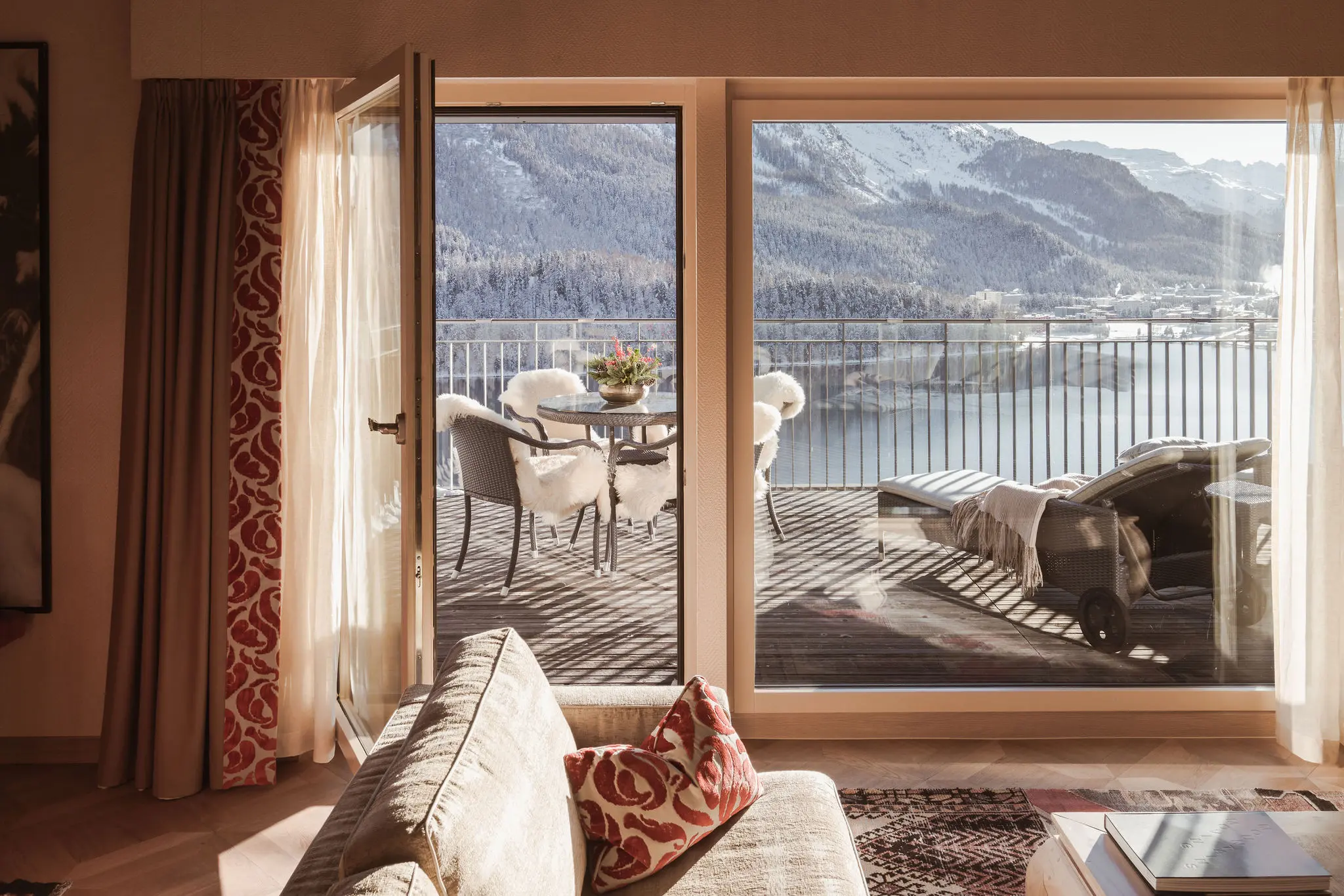 Sunny Carlton Penthouse balcony with outdoor seating, sheepskin throws, and panoramic views of frozen Lake St. Moritz and Engadine mountains