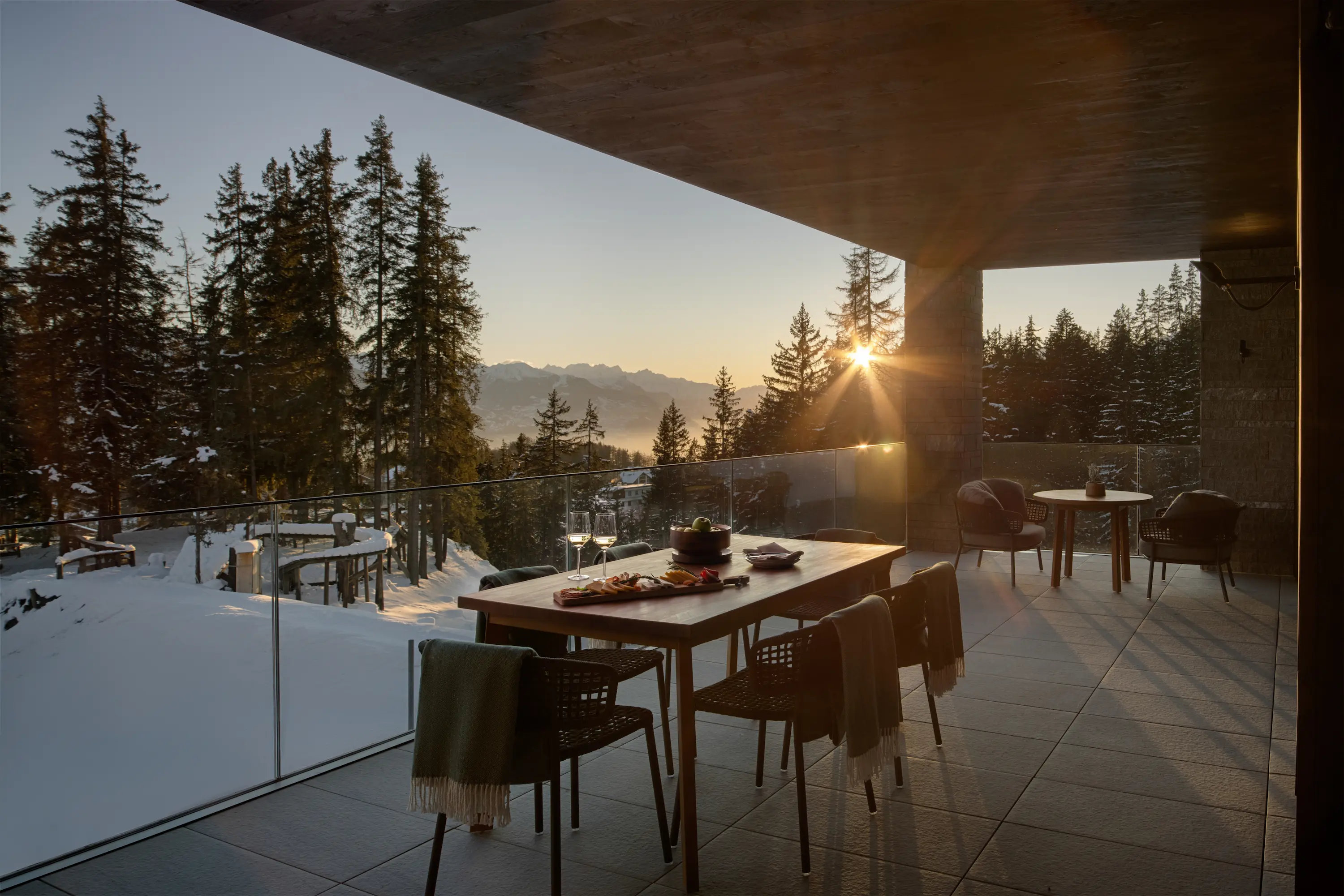 Private suite terrace at Six Senses Crans-Montana with breakfast setup, glass railings, and golden sunrise over snow-covered alpine valley and Valais mountain peaks