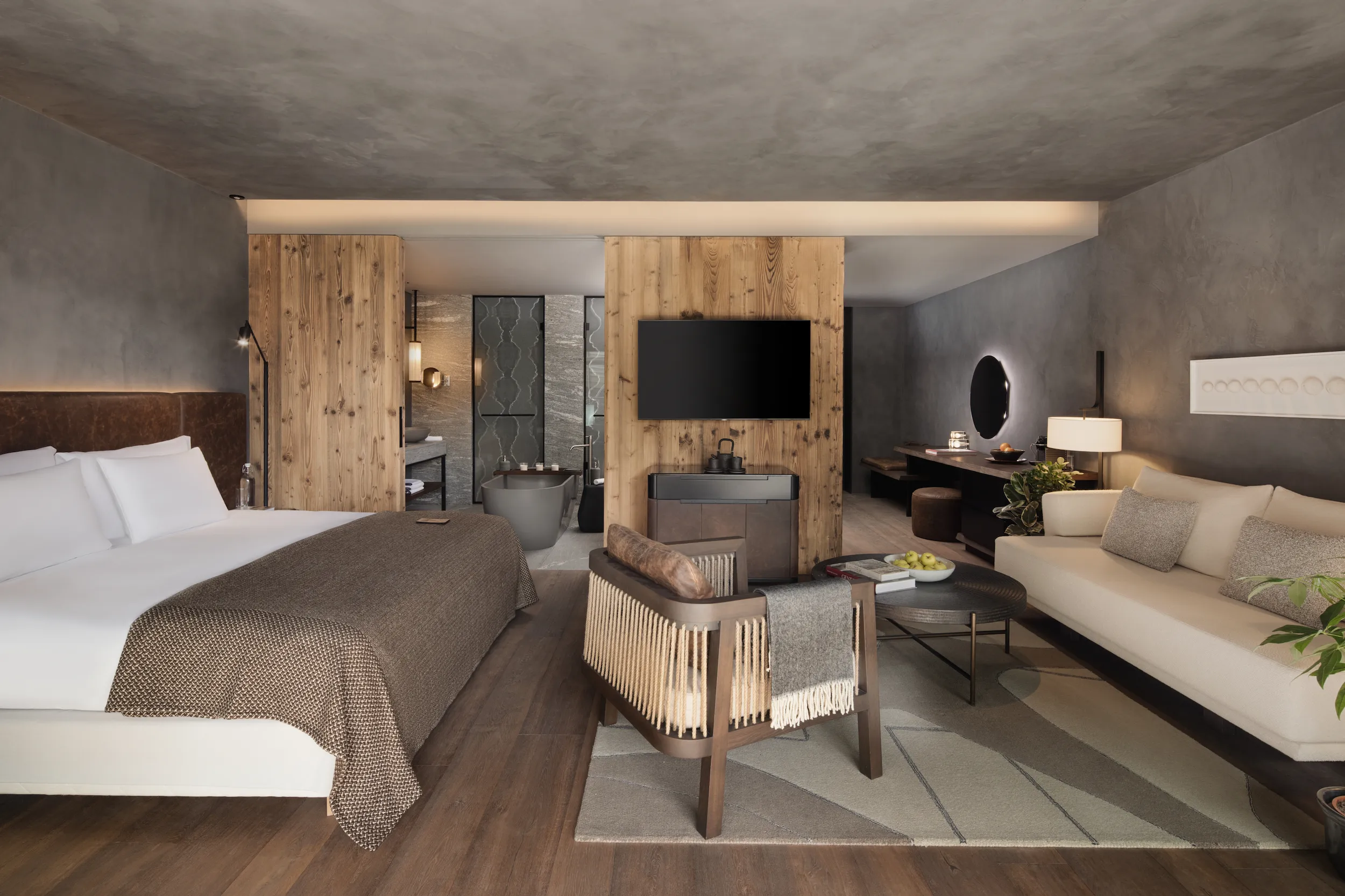 Six Senses Crans-Montana deluxe suite featuring natural larch wood walls, contemporary alpine design, separate living area, and open bathroom with freestanding tub