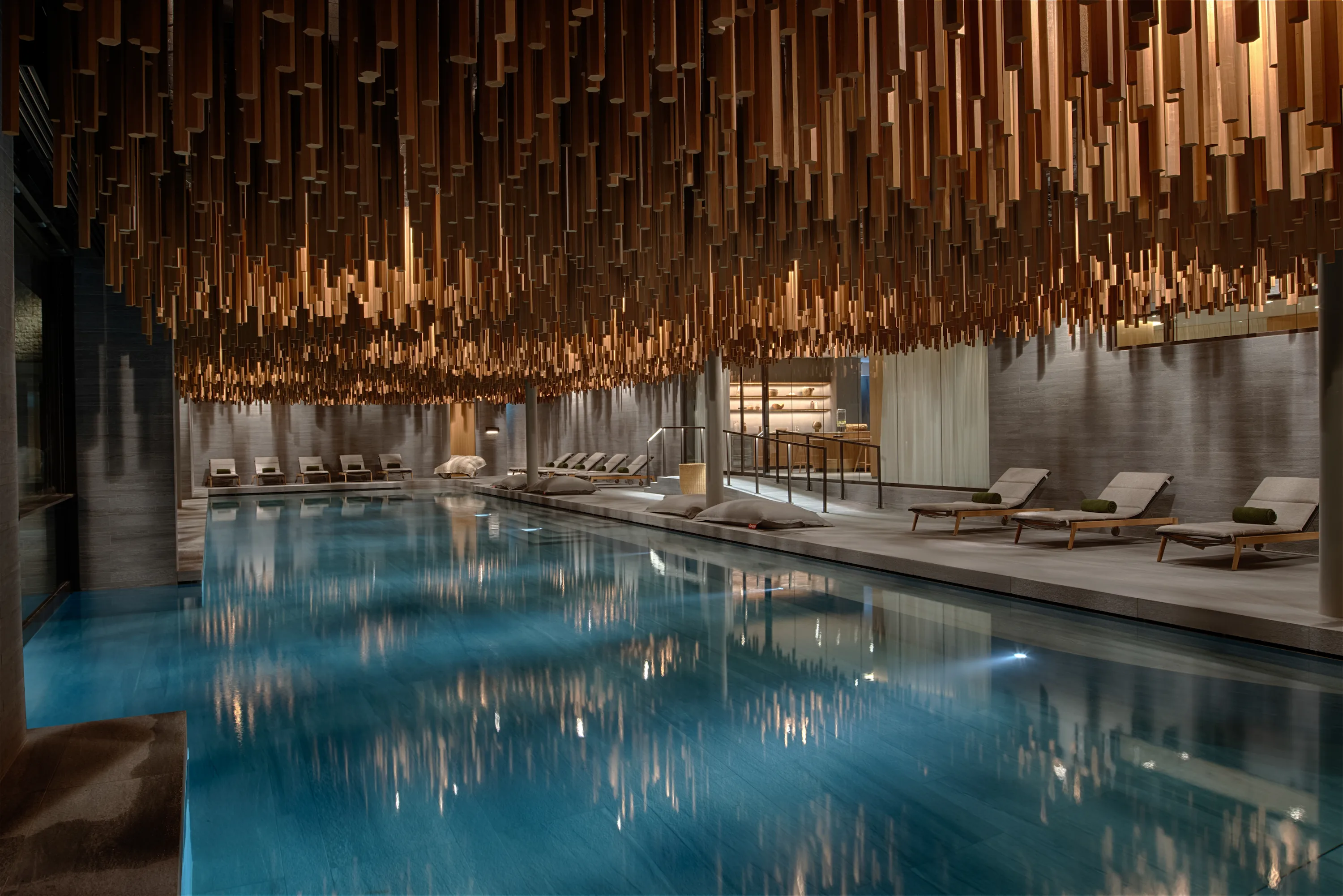 Six Senses Crans-Montana 2,000-m² spa featuring heated indoor pool with dramatic suspended wooden ceiling installation, loungers, and serene minimalist design