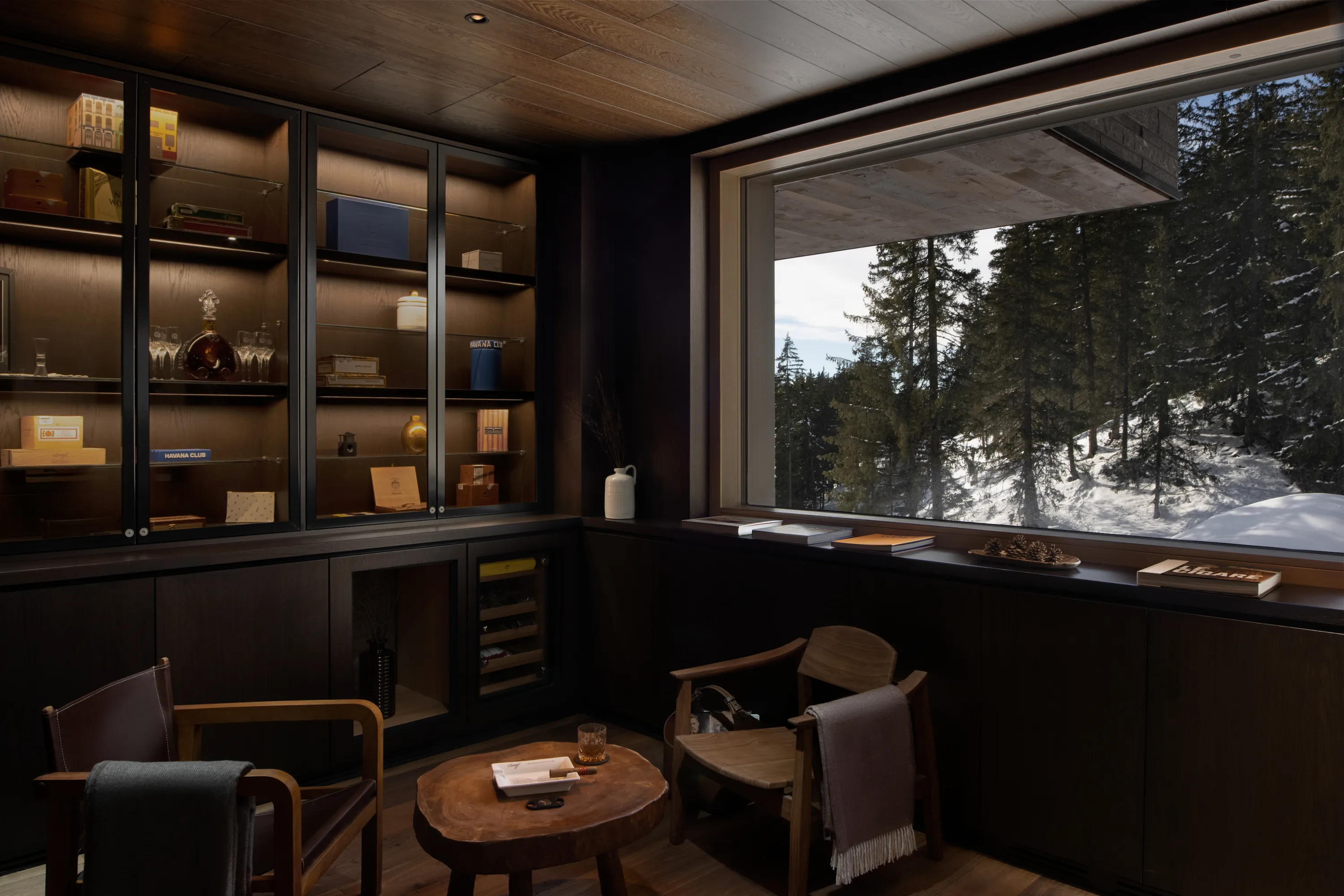 Ora Bar cigar and cognac lounge at Six Senses Crans-Montana featuring dark wood paneling, illuminated display cabinets, intimate seating, and panoramic alpine forest views