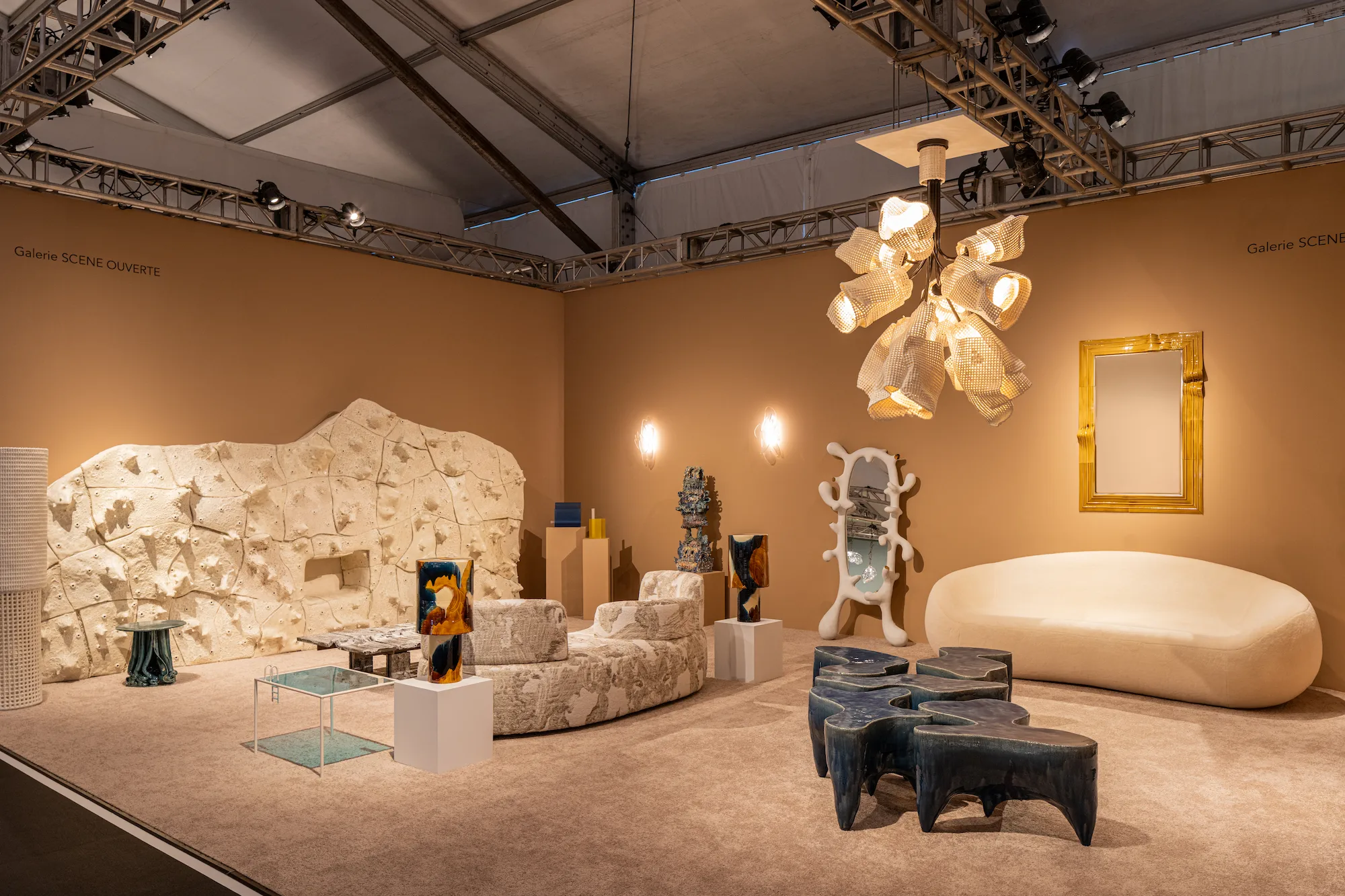 Galerie SCENE OUVERTE booth at Design Miami 2025 with warm ochre walls displaying Simone Crestani blown glass works, textured stone furniture, sculptural chandelier, and contemporary collectible design