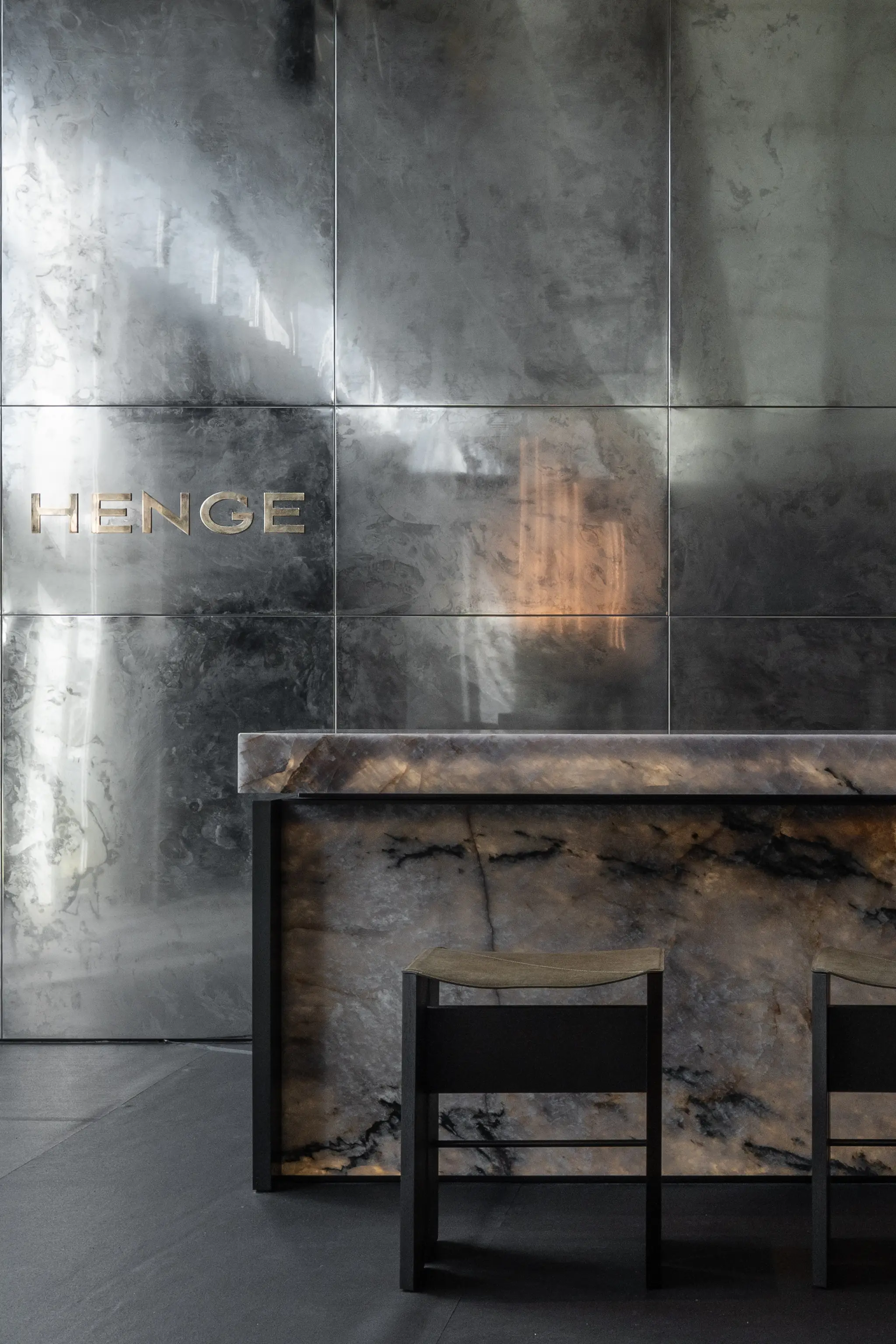 Henge Collectors Lounge at Design Miami 2025 featuring textured pale gold metal wall panels with engraved Henge branding and sculptural stone table with black metal seating