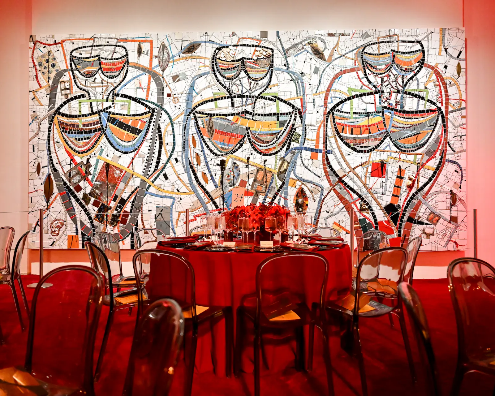 Elegant dinner table with red floral centerpiece set against large-scale colorful mosaic artwork featuring abstract figures at Guggenheim Museum 2025 benefit gala