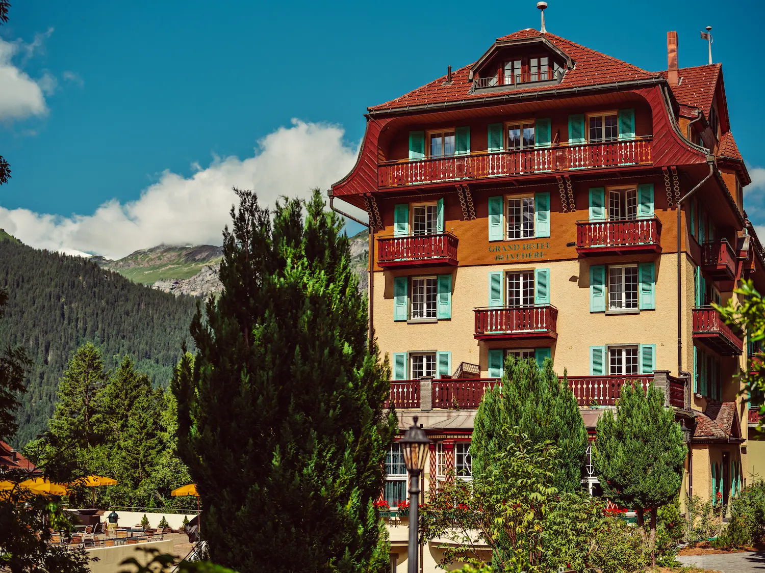 Grand Hotel Belvedere historic 1912 Belle Époque facade with traditional red balconies and turquoise shutters in Wengen, Switzerland with Alpine mountain backdrop