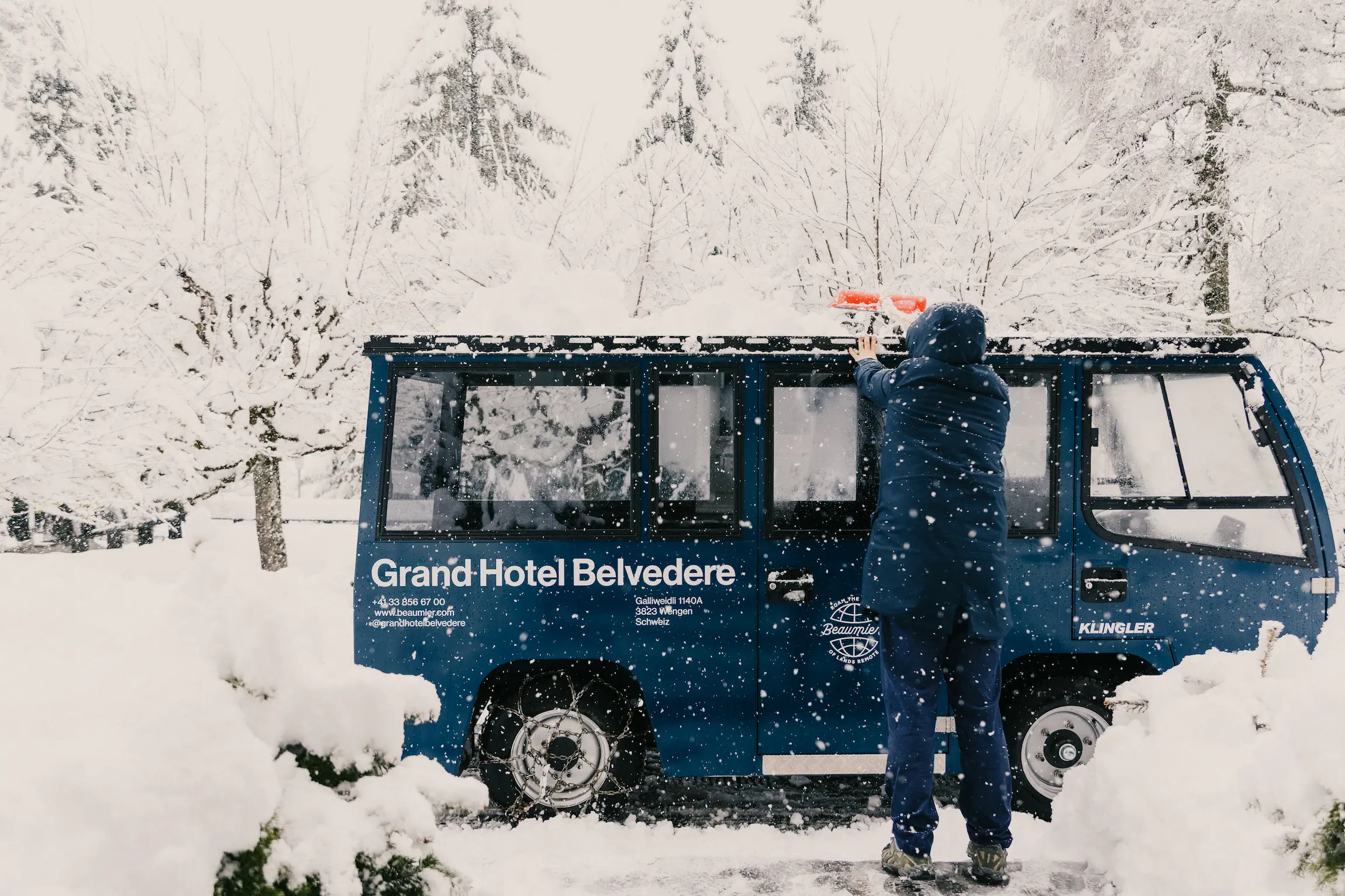 Grand Hotel Belvedere branded shuttle vehicle being cleared of snow in car-free Wengen village during winter snowfall in Swiss Alps
