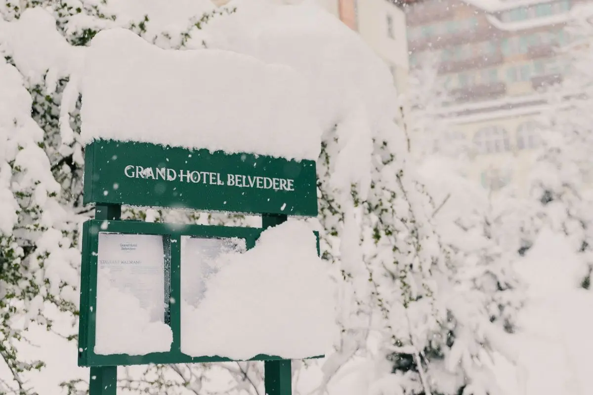 Snow-covered Grand Hotel Belvedere entrance sign with historic Belle Époque building visible through winter snowfall in Wengen, Bernese Oberland