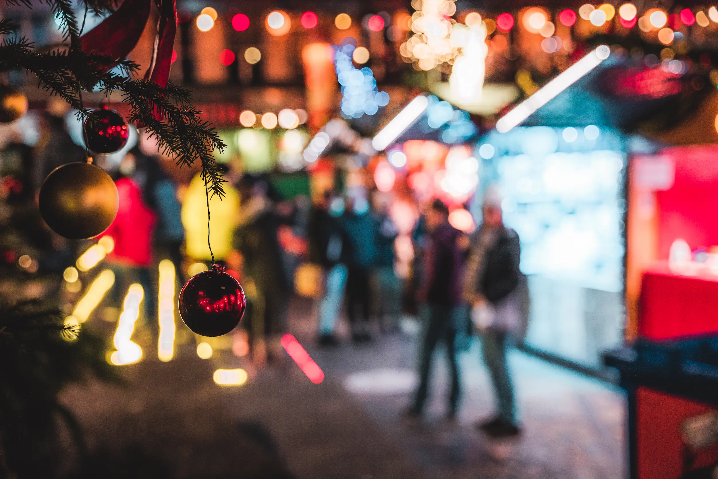 Close-up of Christmas tree ornaments with colorful bokeh lights from market stalls creating festive atmosphere at Swiss Christmas market with blurred visitors in background
