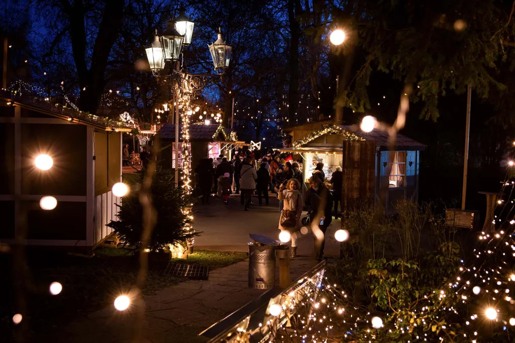 Illuminated pathways with vintage street lamps and string lights leading through wooden chalets at Bern Sternenmarkt Star Market Christmas village at night