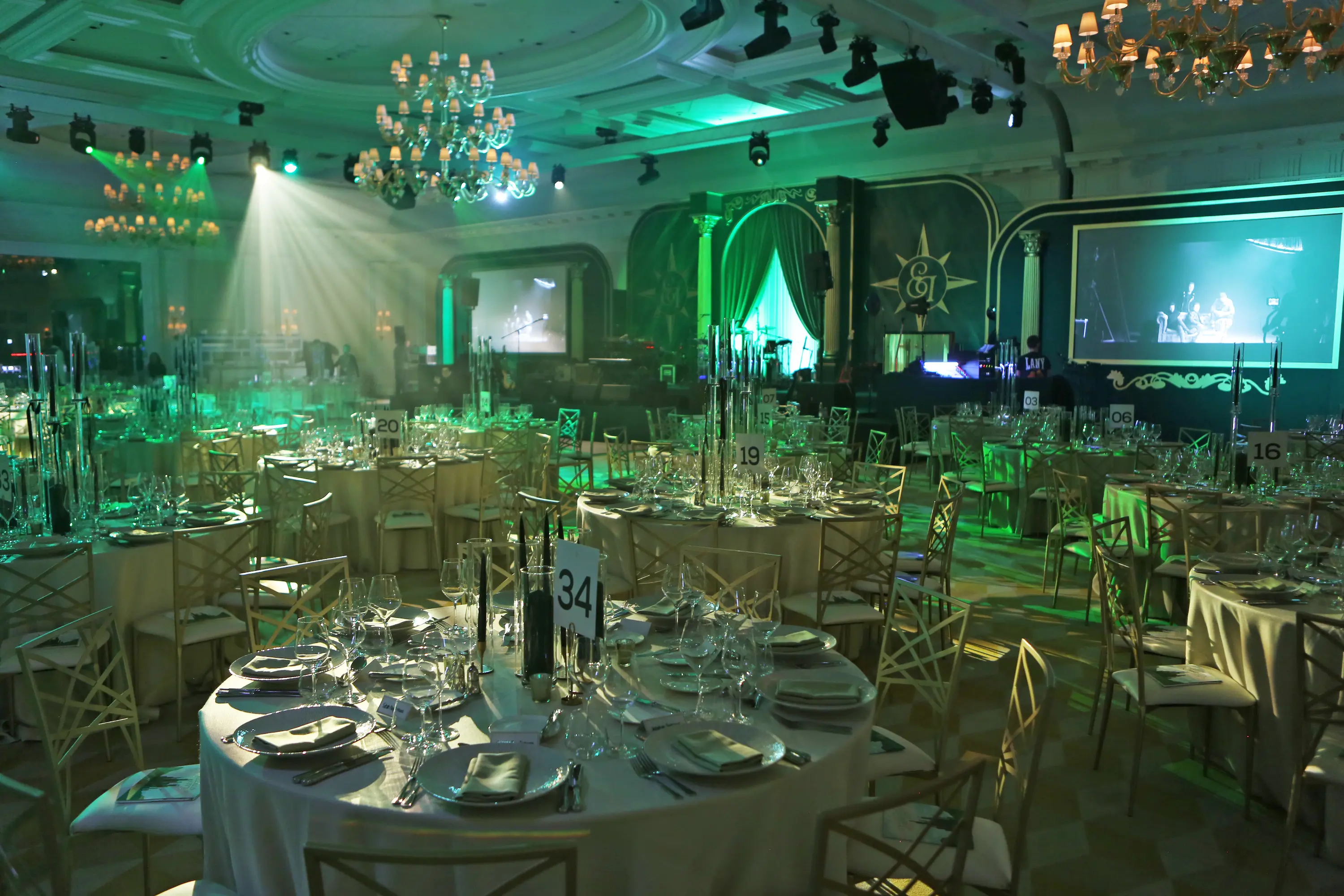 Elegant ballroom setup with round dining tables, crystal chandeliers, and signature emerald lighting at Emeralds & Ivy Ball 2025 for Cancer Research UK at Raffles London The OWO