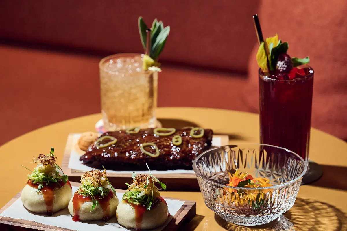 Inventive cocktails with botanical garnishes alongside glazed duck appetizers and artisanal amuse-bouche on round table at IGNIV Andermatt sharing experience by Chef Valentin Sträuli