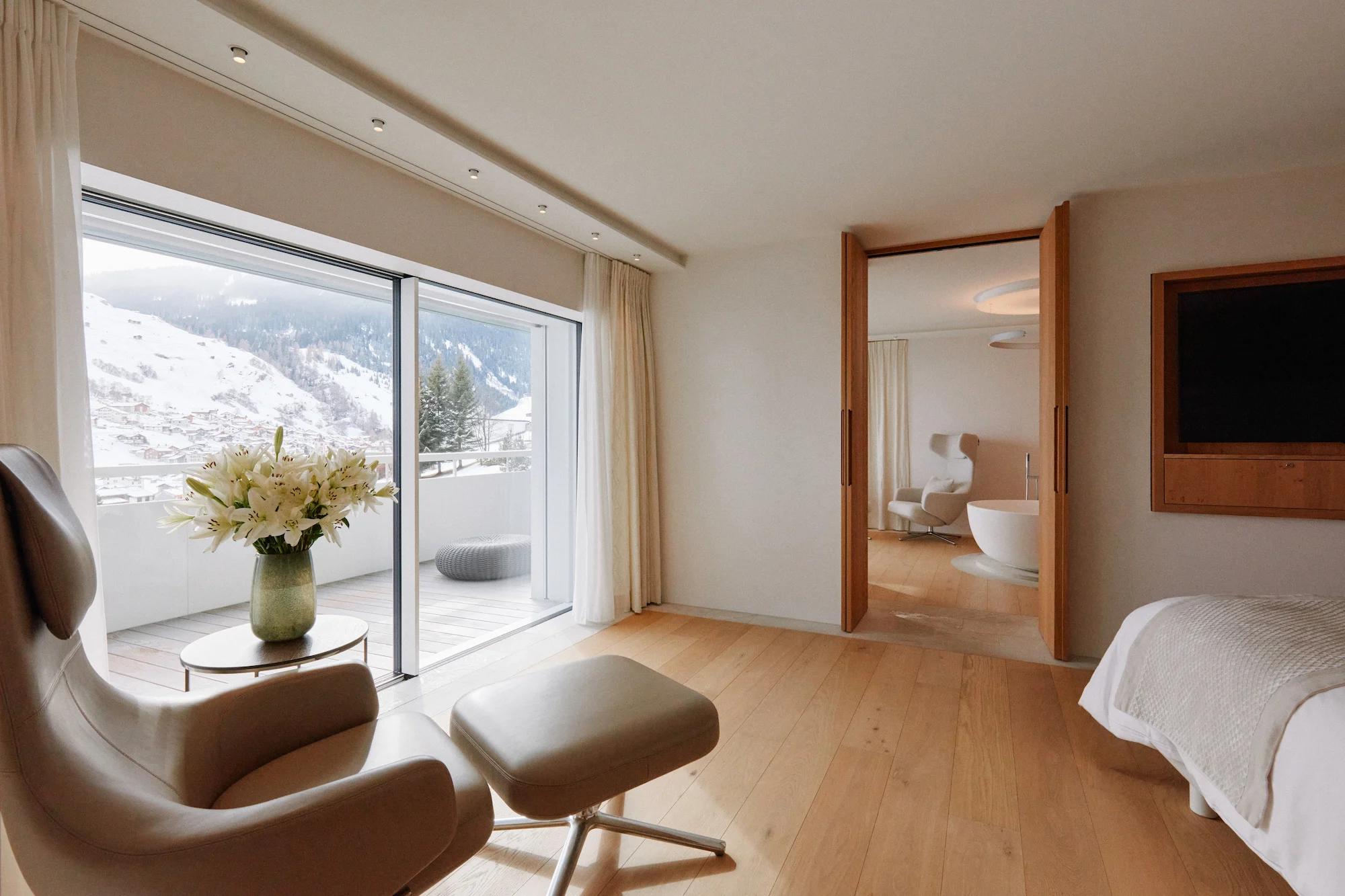 Luxury penthouse suite with oak flooring, designer lounge chair, private balcony overlooking snow-covered Vals village designed by Pritzker Prize winner Kengo Kuma at 7132 Hotel