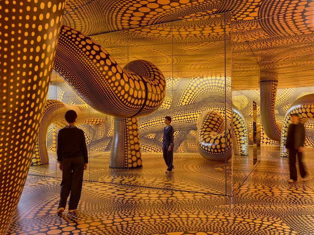 Visitors inside Yayoi Kusama's golden Infinity Mirrored Room installation with polka dot pumpkin sculptures at Fondation Beyeler