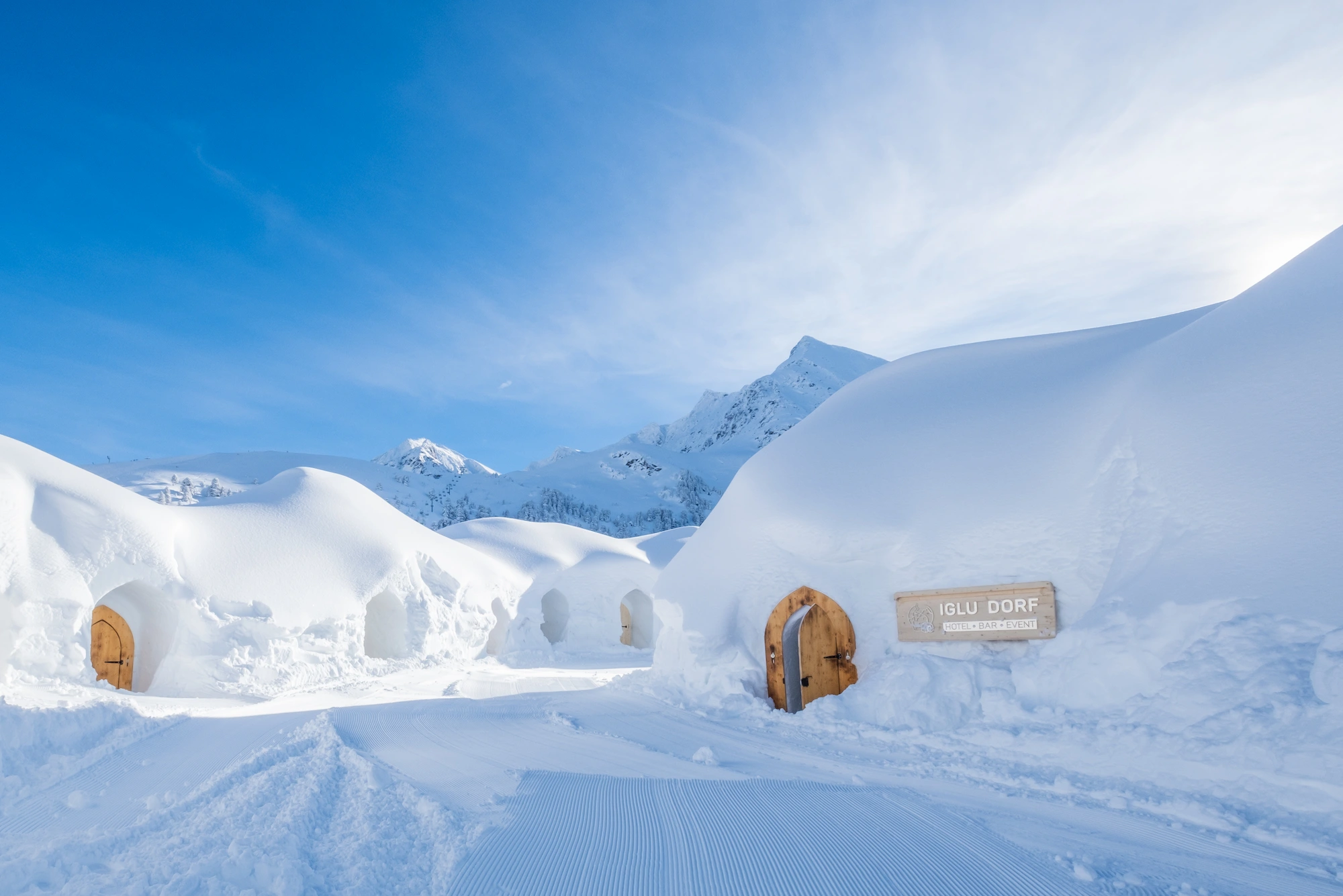 Iglu Dorf ice hotel village with carved wooden doors and arched snow corridors against alpine mountain backdrop in Gstaad Switzerland