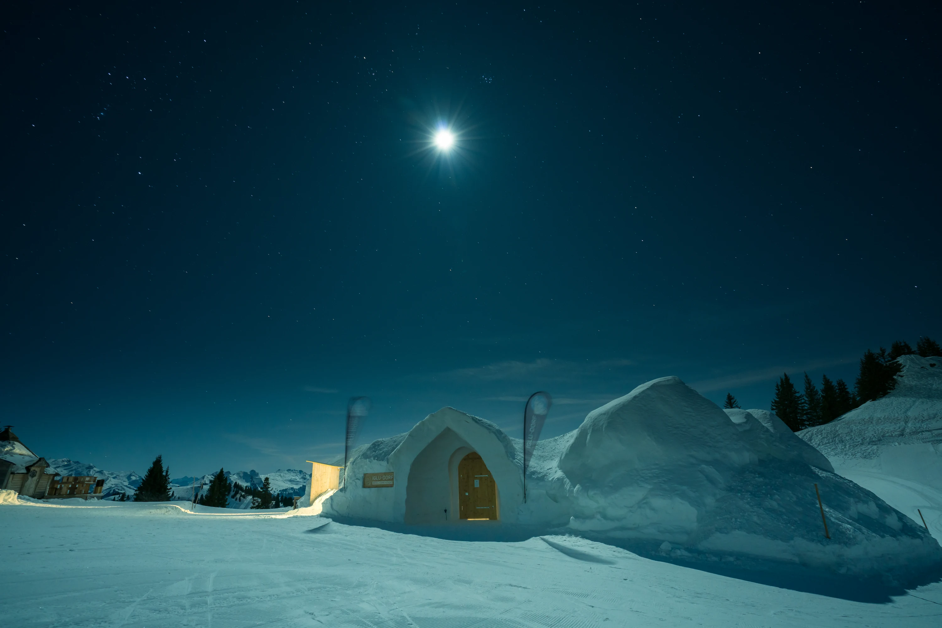 Igloo Dorf Gstaad ice hotel illuminated under full moon and starry night sky in Swiss Alps Bernese Oberland winter