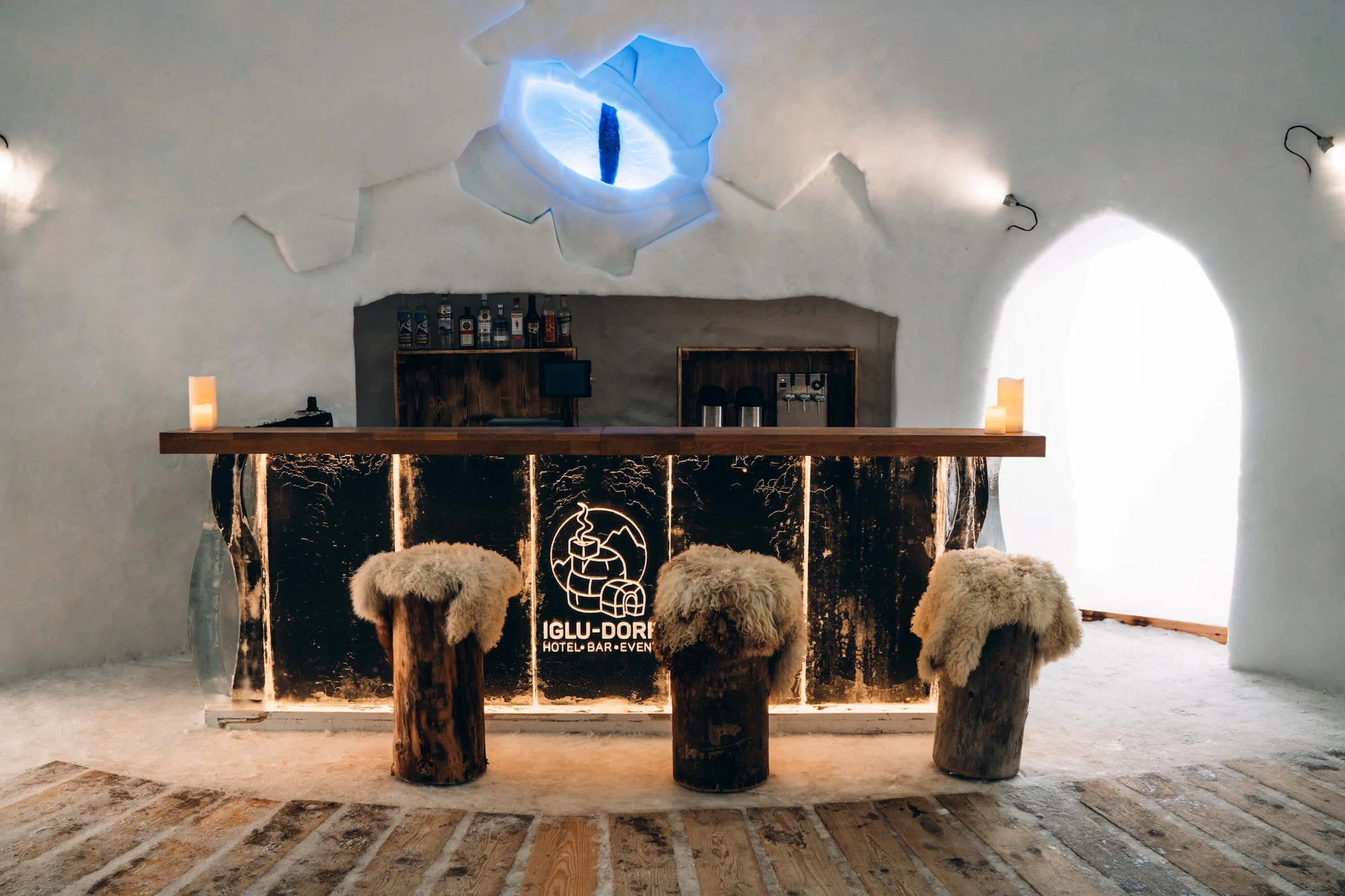Iglu Dorf Gstaad ice bar interior with rustic wooden counter sheepskin stools and blue ice sculpture lighting in Swiss Alps