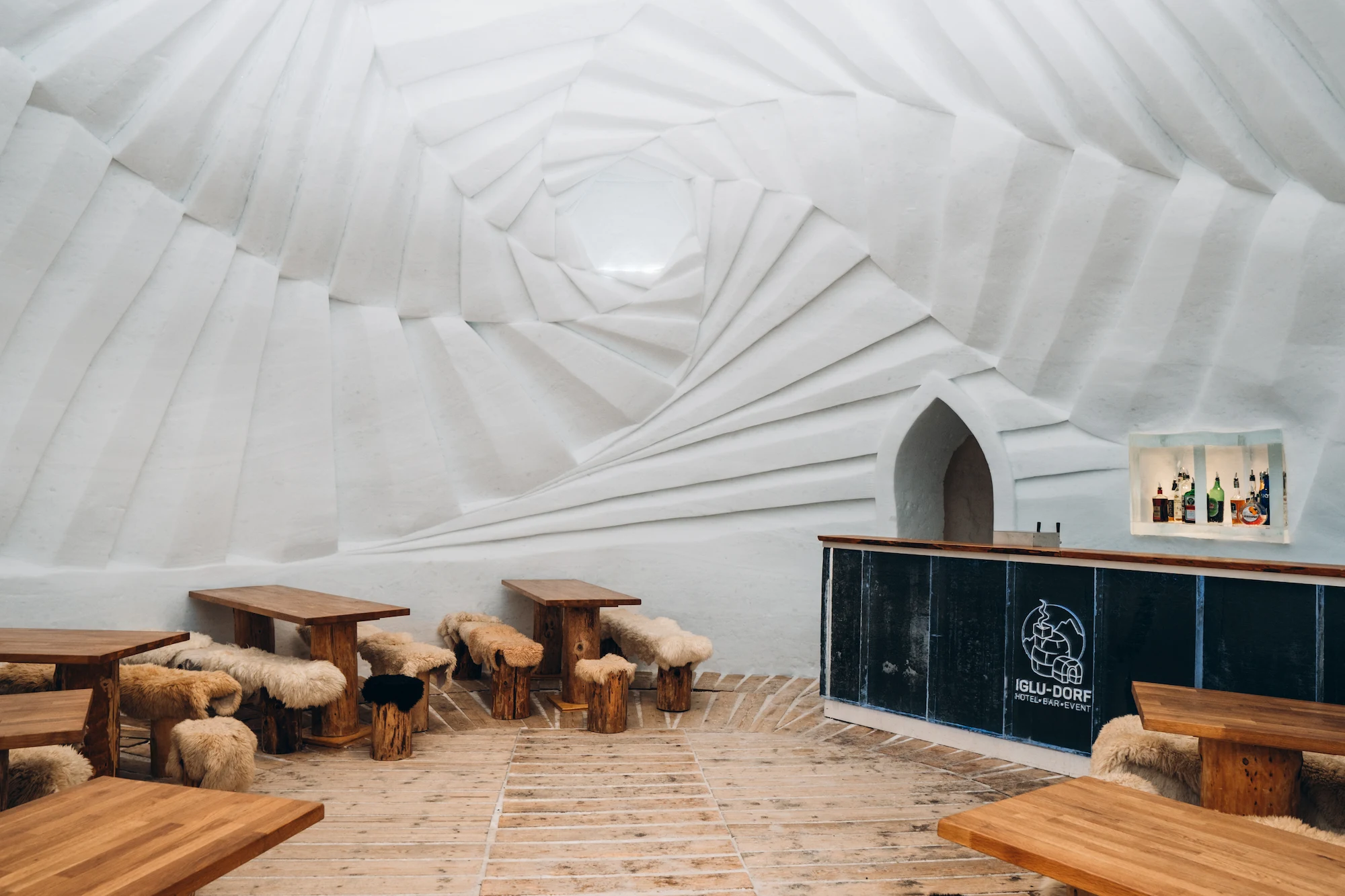 Iglu Dorf Gstaad communal dining hall featuring dramatic spiral carved ice ceiling wooden tables with sheepskin seating and rustic bar
