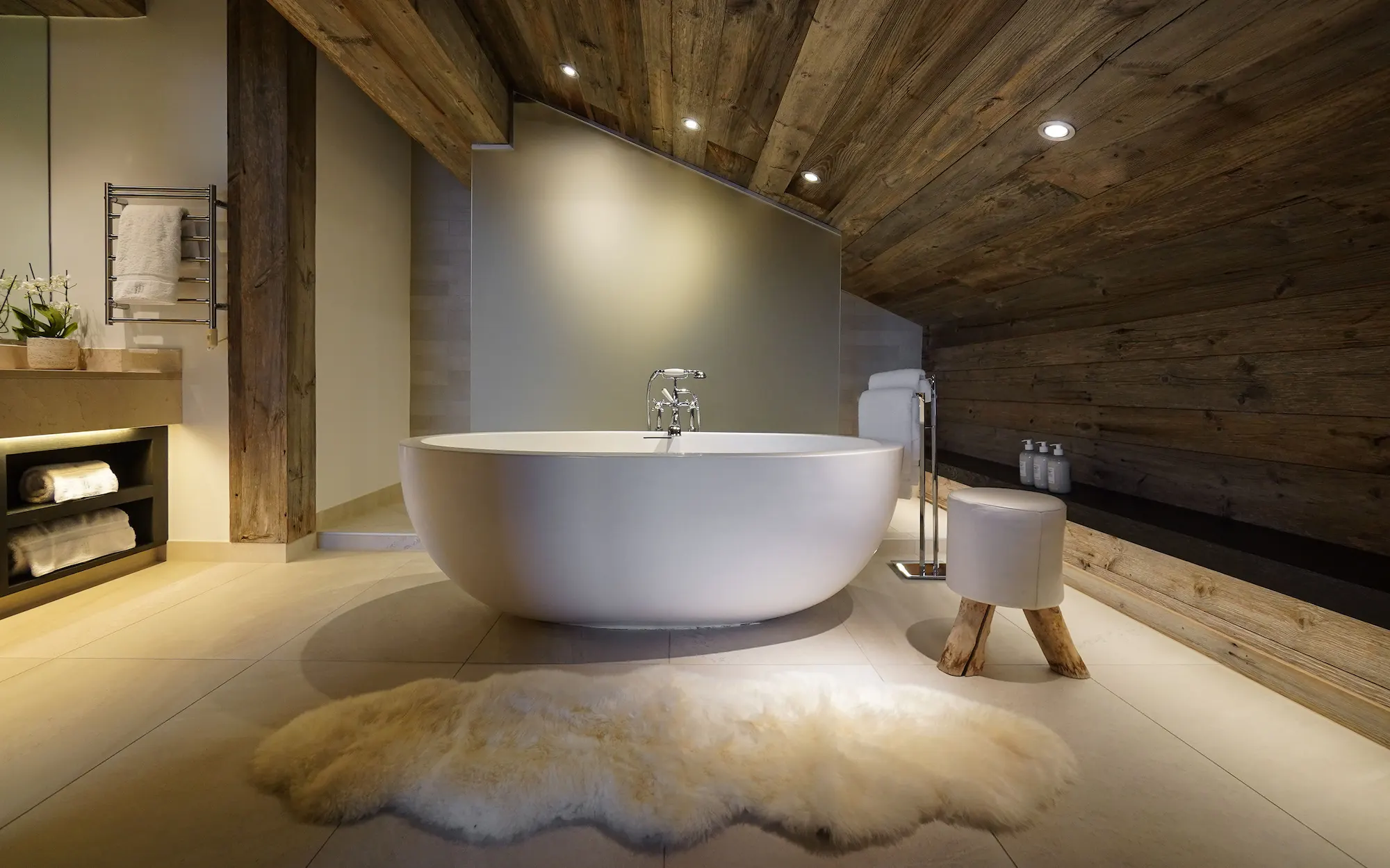Spa-inspired master suite bathroom at The Lodge Verbier featuring freestanding soaking tub sheepskin rug and reclaimed wood beamed ceiling