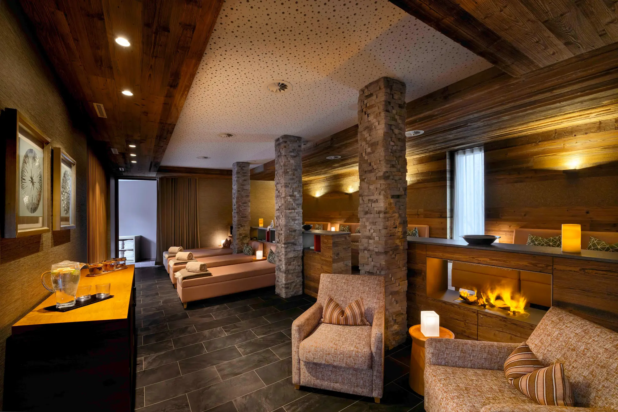 Peak Health Spa relaxation room at The Capra with massage beds stone pillars fireplace and ambient lighting for holistic wellness treatments