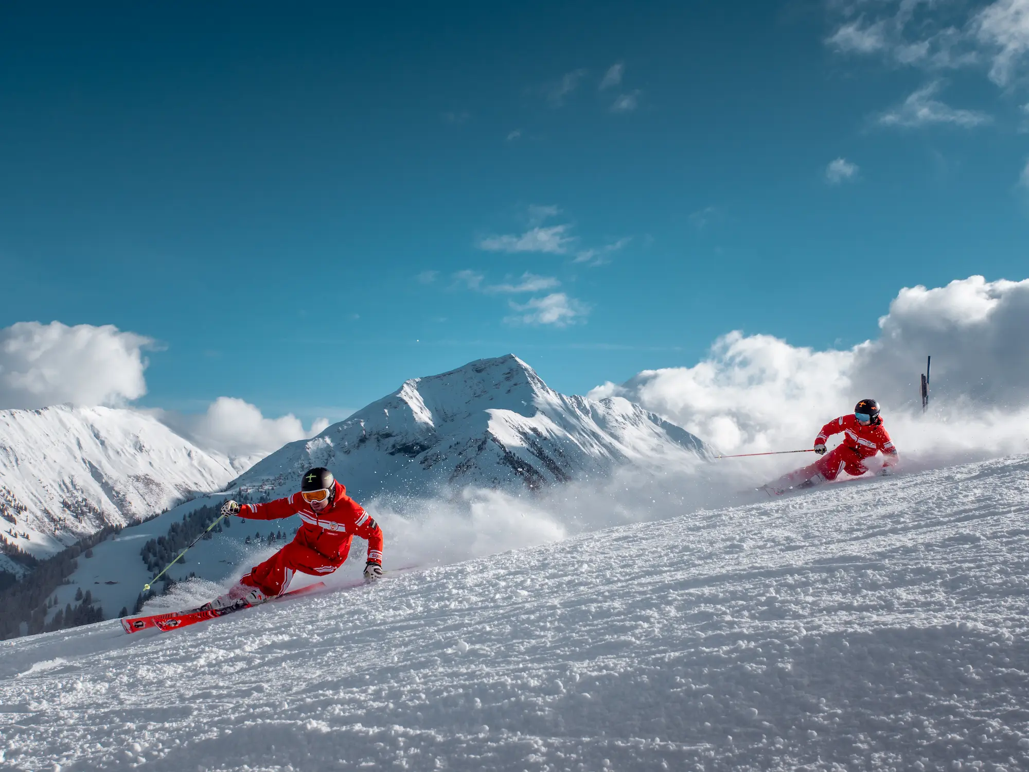 Ski School Rougemont instructors in red uniforms carving fresh tracks on groomed pistes with dramatic Bernese Oberland peaks backdrop in Gstaad region Switzerland