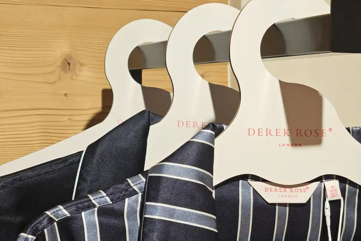 Derek Rose luxury navy striped silk pyjamas on branded hangers displayed against natural wood paneling in Gstaad boutique