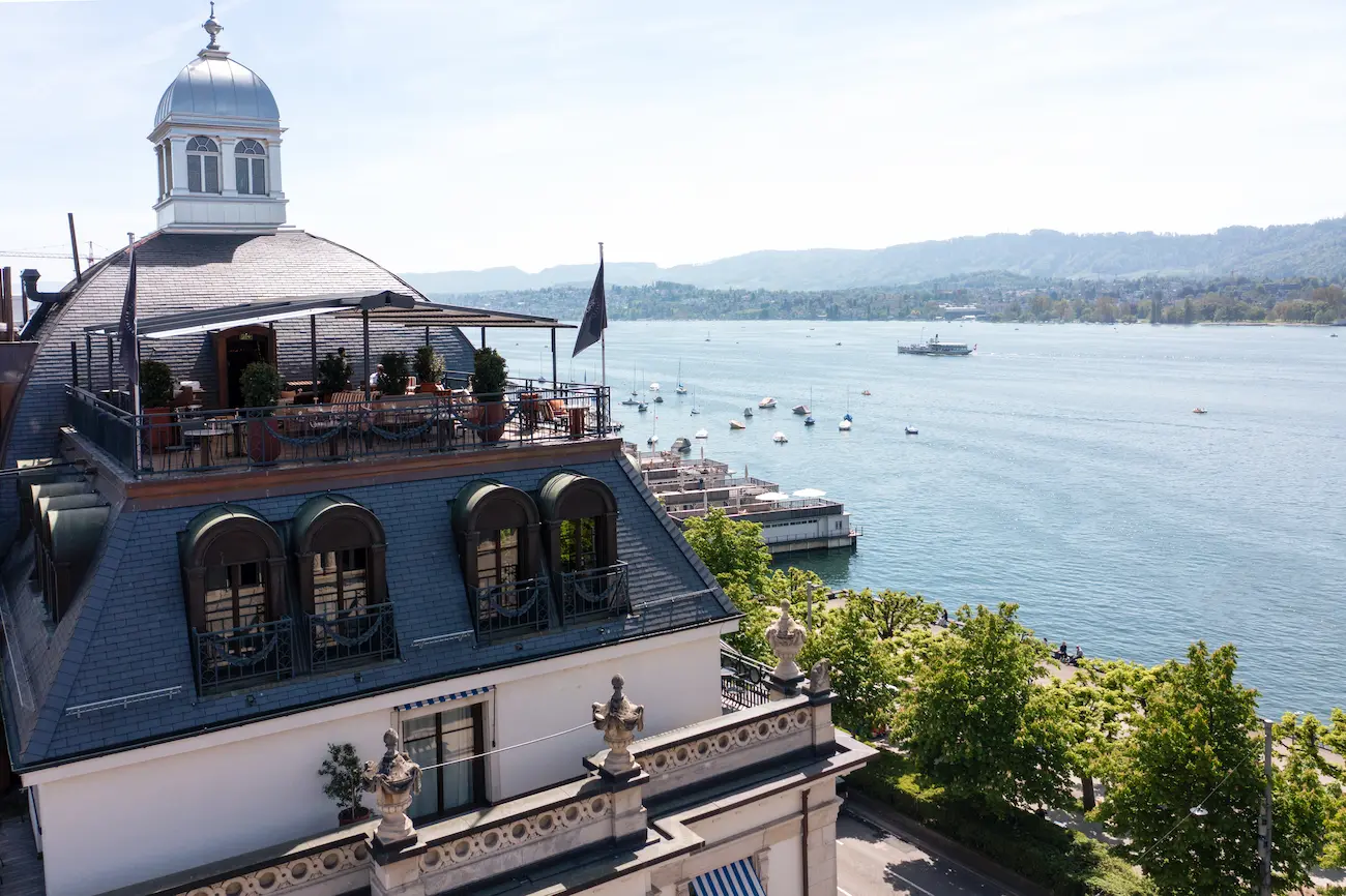 Panoramic rooftop terrace at La Muña restaurant overlooking Lake Zurich with sailboats, Alpine foothills, dome cupola, and sixth-floor dining terrace at La Réserve Eden au Lac