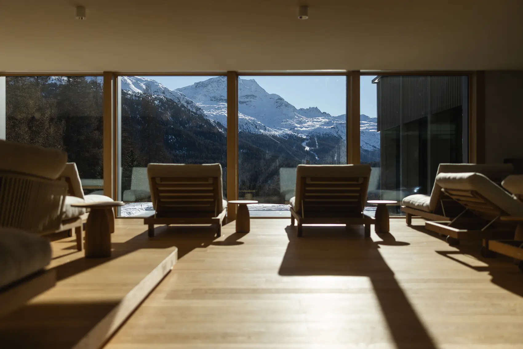 Serene spa relaxation lounge at Suvretta House St. Moritz featuring wooden sun loungers facing floor-to-ceiling windows with breathtaking panoramic views of snow-covered Alpine peaks, showcasing the five-star hotel's premium wellness facilities and mountai