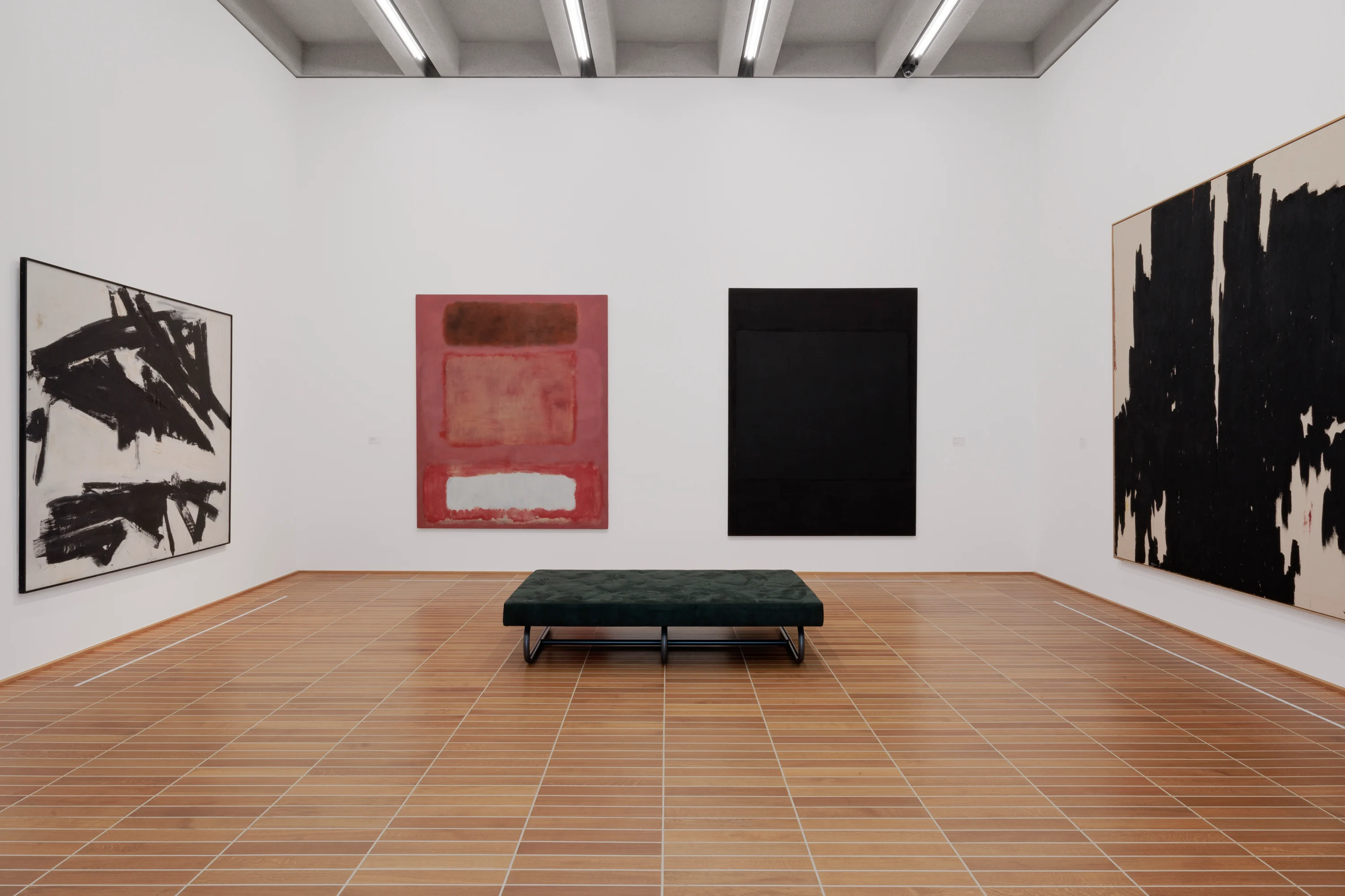 Abstract expressionist art gallery with large-scale paintings including Mark Rothko red color field work and Franz Kline black gestural abstractions on white walls, green tufted bench on terracotta tile floor, exposed beam ceiling