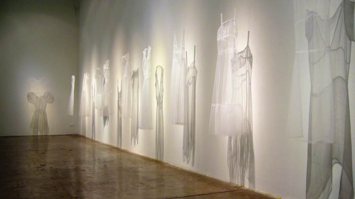 Ethereal contemporary art installation featuring suspended translucent white fabric garments and forms arranged along white gallery wall with dramatic backlighting creating ghostly shadows