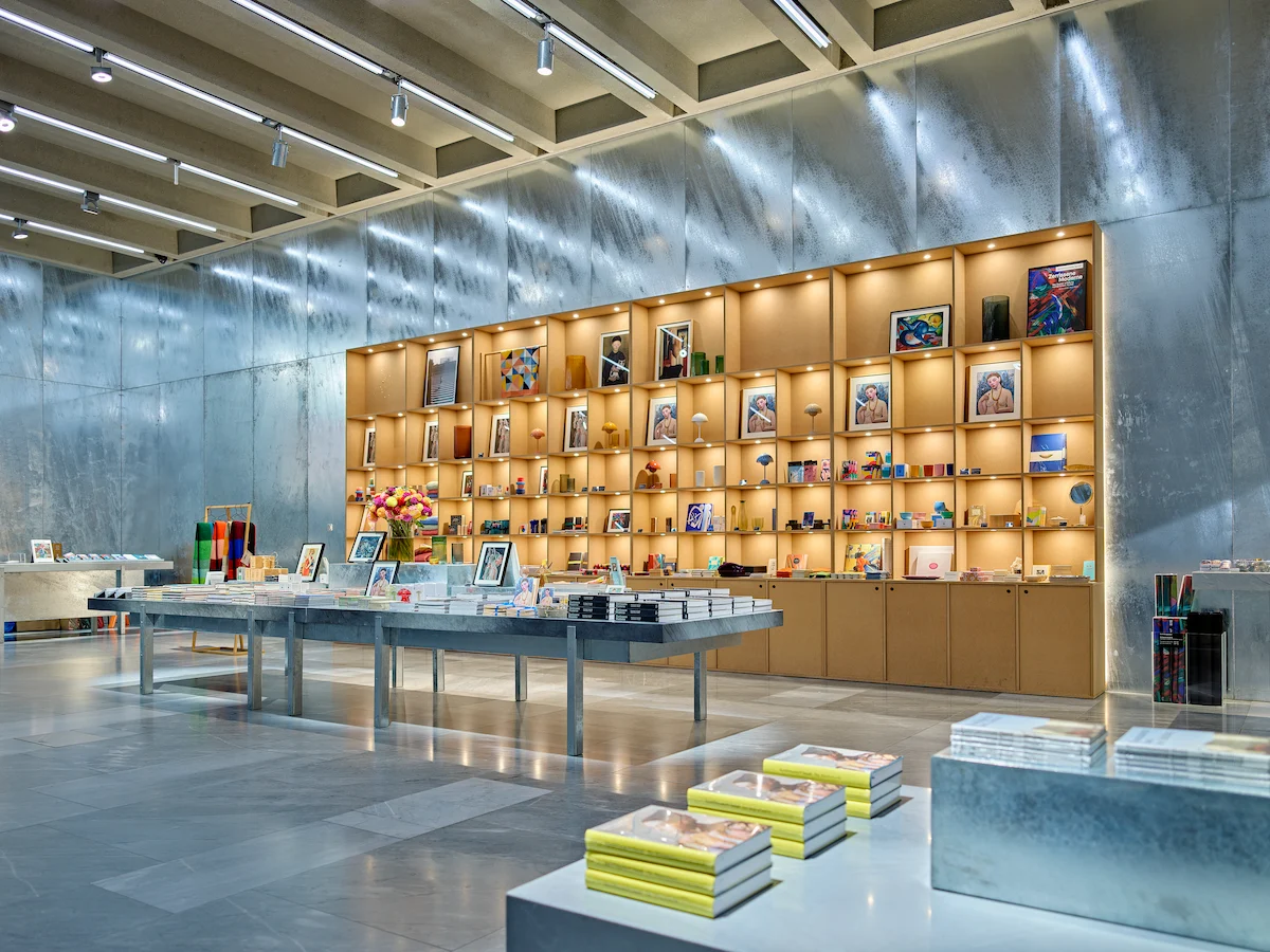 Modern museum shop interior at Kunstmuseum Basel featuring illuminated blonde wood cubic shelving system displaying art books