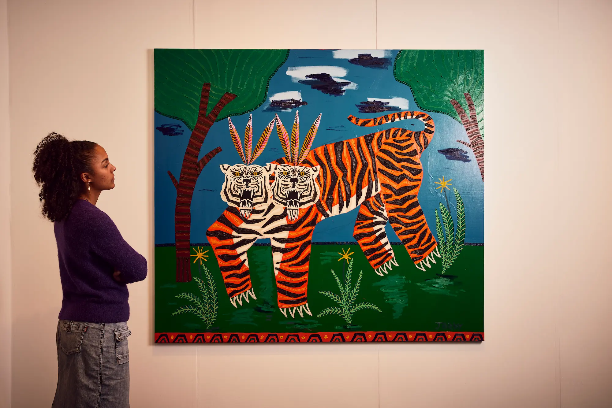 Visitor viewing vibrant contemporary folk art painting of orange and black striped two-headed tiger with decorative palm trees and tropical foliage against blue sky and green landscape at London Art Fair 2026