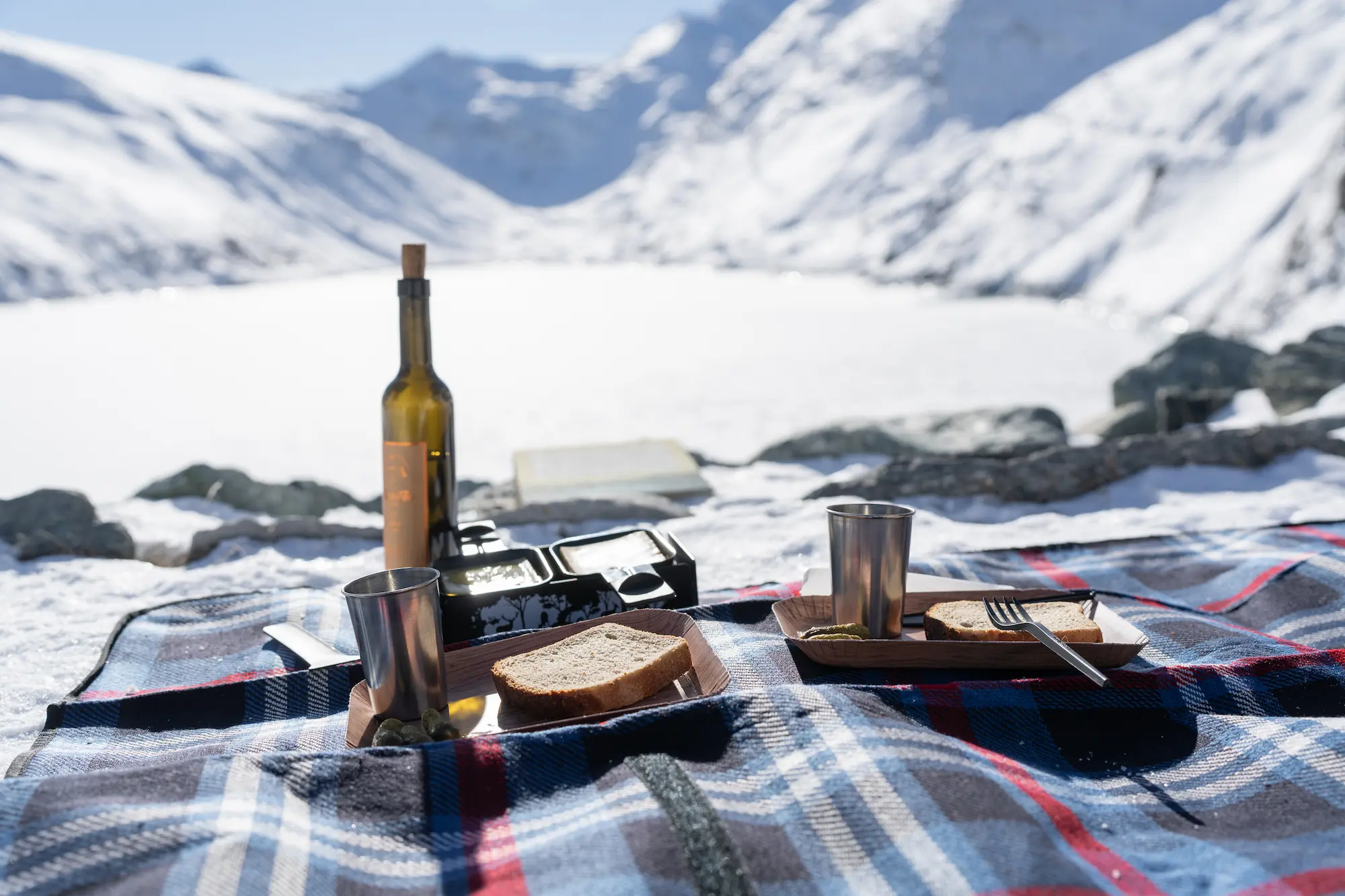 Elegant glacier picnic setup on plaid blanket at Saas-Fee featuring traditional Swiss raclette cheese with bread